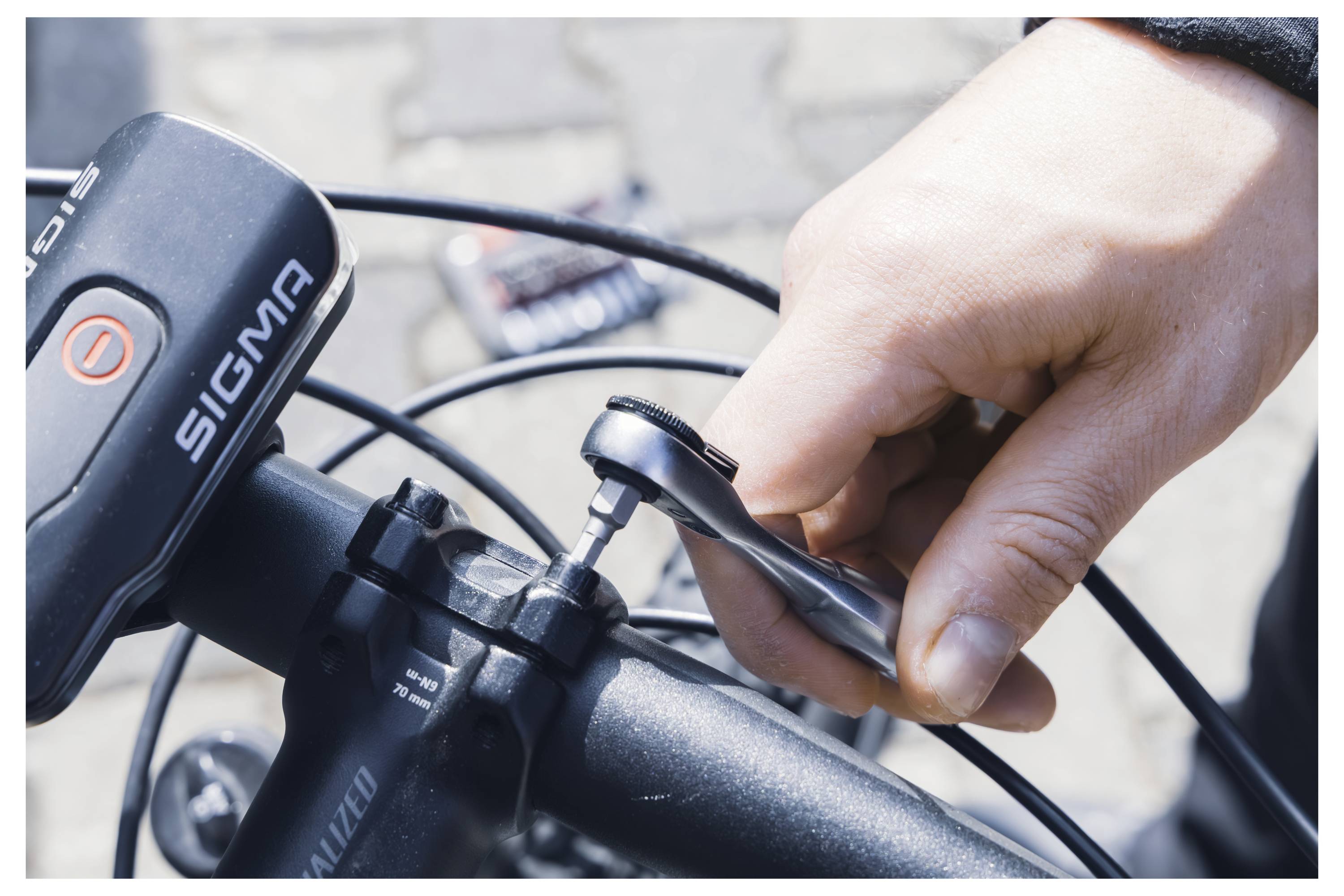 A person tightens a bolt on a bicycle handlebar using an Allen wrench. The bike has a Sigma bike computer attached.