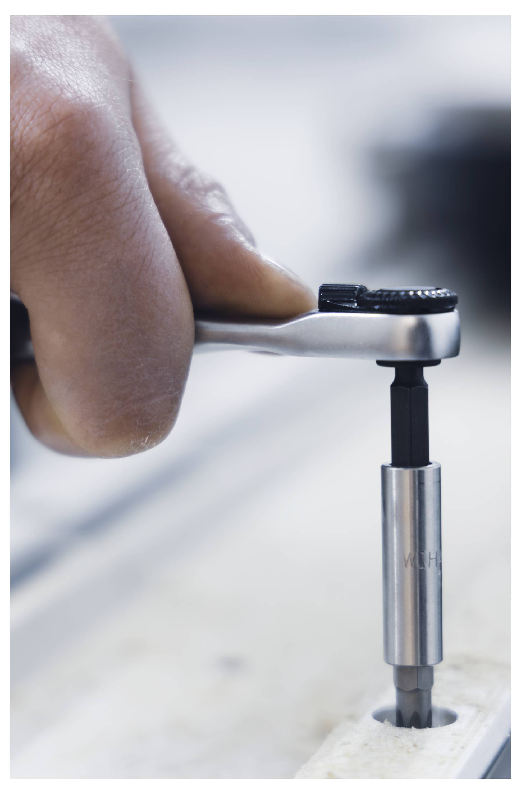 A hand uses a ratchet wrench to tighten or loosen a screw in a mechanical component, illustrating precise adjustment in a workshop setting.