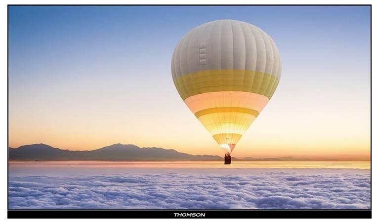A hot air balloon soars above a cloud-covered landscape at sunrise, with distant mountains on the horizon.