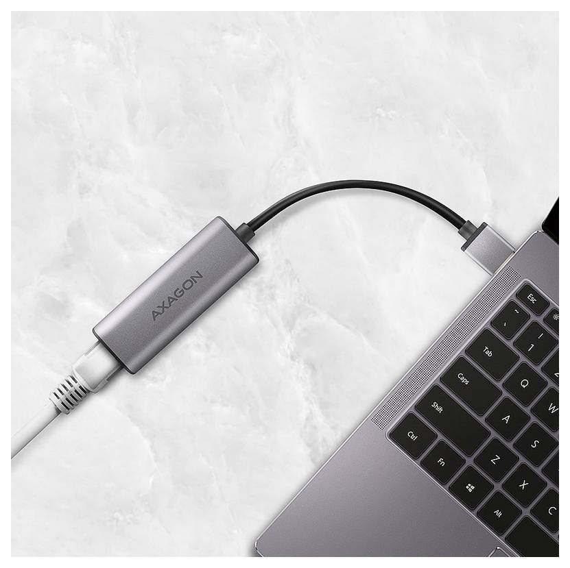 USB-C adapter connected to a laptop, linking a white cable to the computer on a light marble surface.