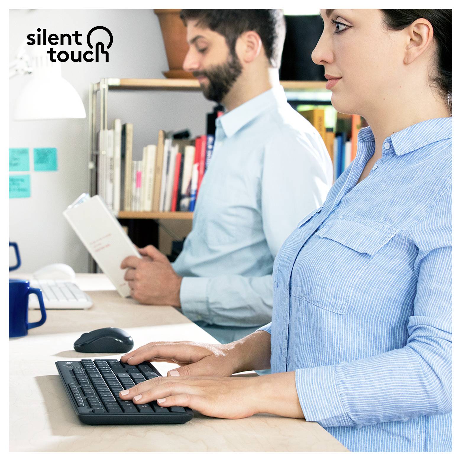 Office workers at desks, with a woman typing on a keyboard in the foreground and a man reading a document behind her.