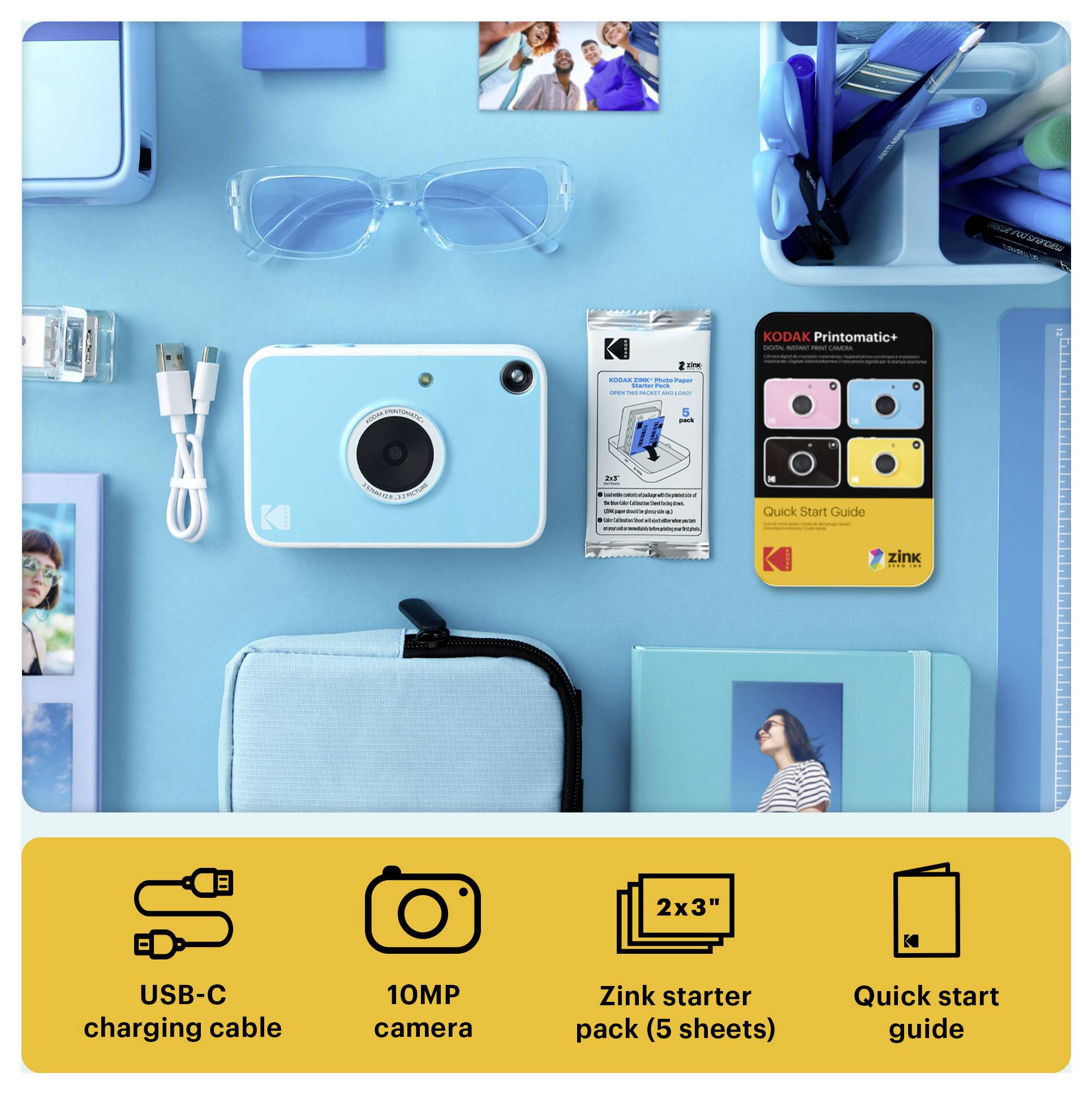 Flat lay of a Kodak instant camera kit on a blue background, showing the camera, USB-C cable, glasses, Zink starter pack, quick start guide, and carrying case.
