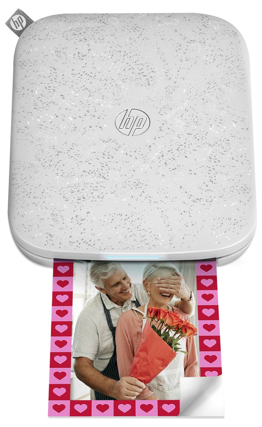 White HP portable photo printer printing a couple's photo framed with pink hearts and a curled corner.