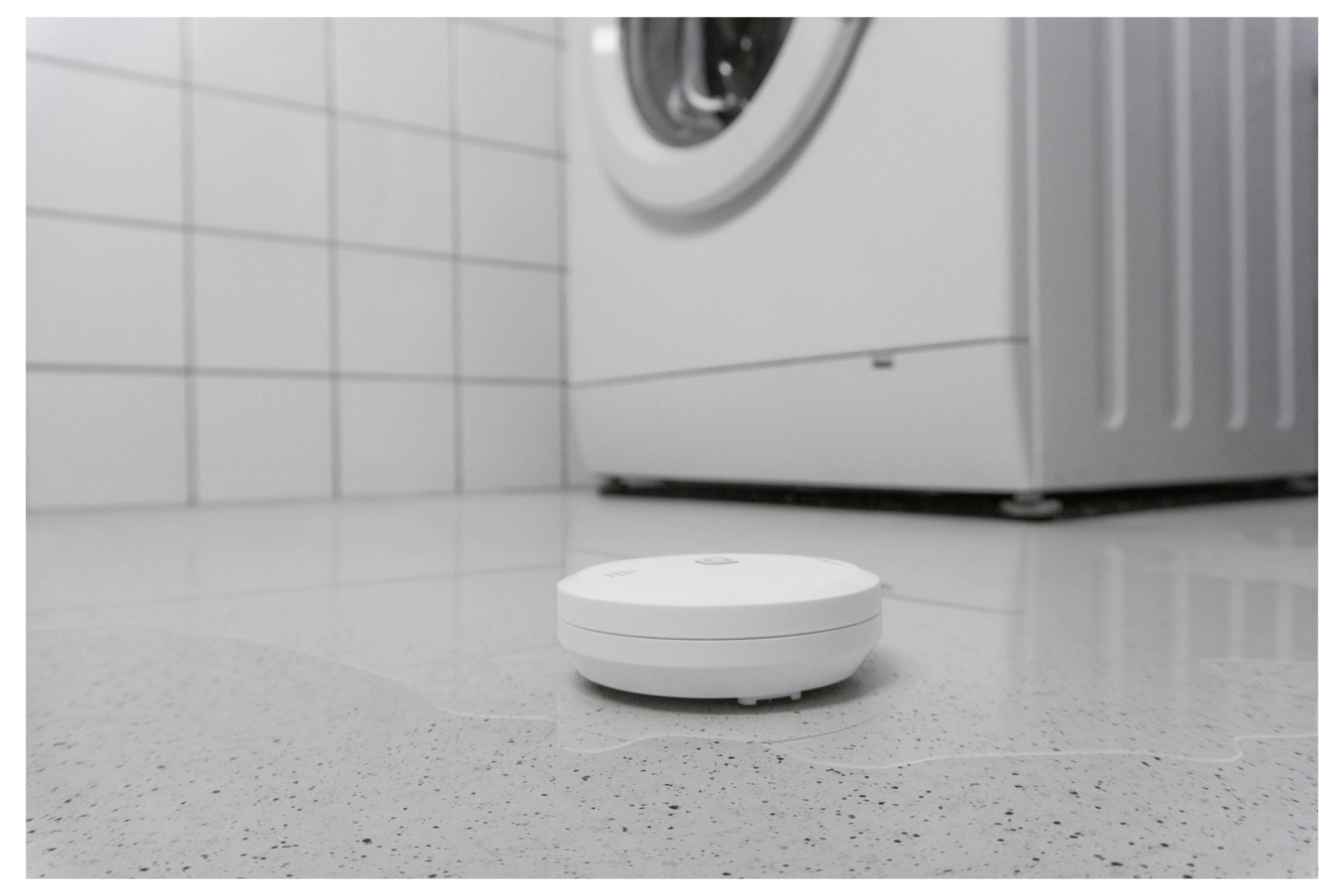 Robot vacuum cleaner on a tiled floor in front of a washing machine in a laundry room