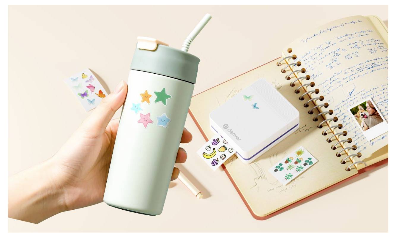 Hand holding a mint green tumbler with a straw and star stickers beside an open notebook, small sticker pack, and pen on a beige desk.