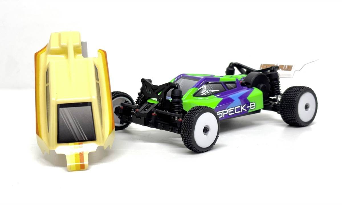 Two RC car bodies on a white background: a yellow shell standing upright beside a black, green, and purple 'SPECK-S' buggy chassis.