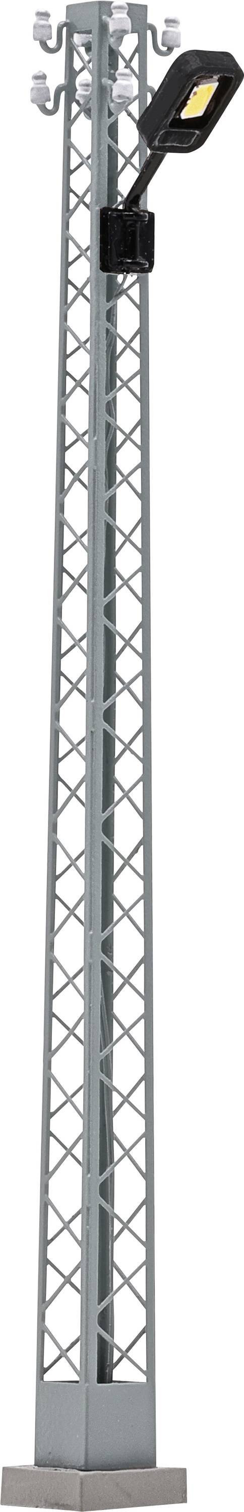 Tall gray lattice tower with a black streetlight fixture and yellow-lit lamp mounted near the top on a concrete base.