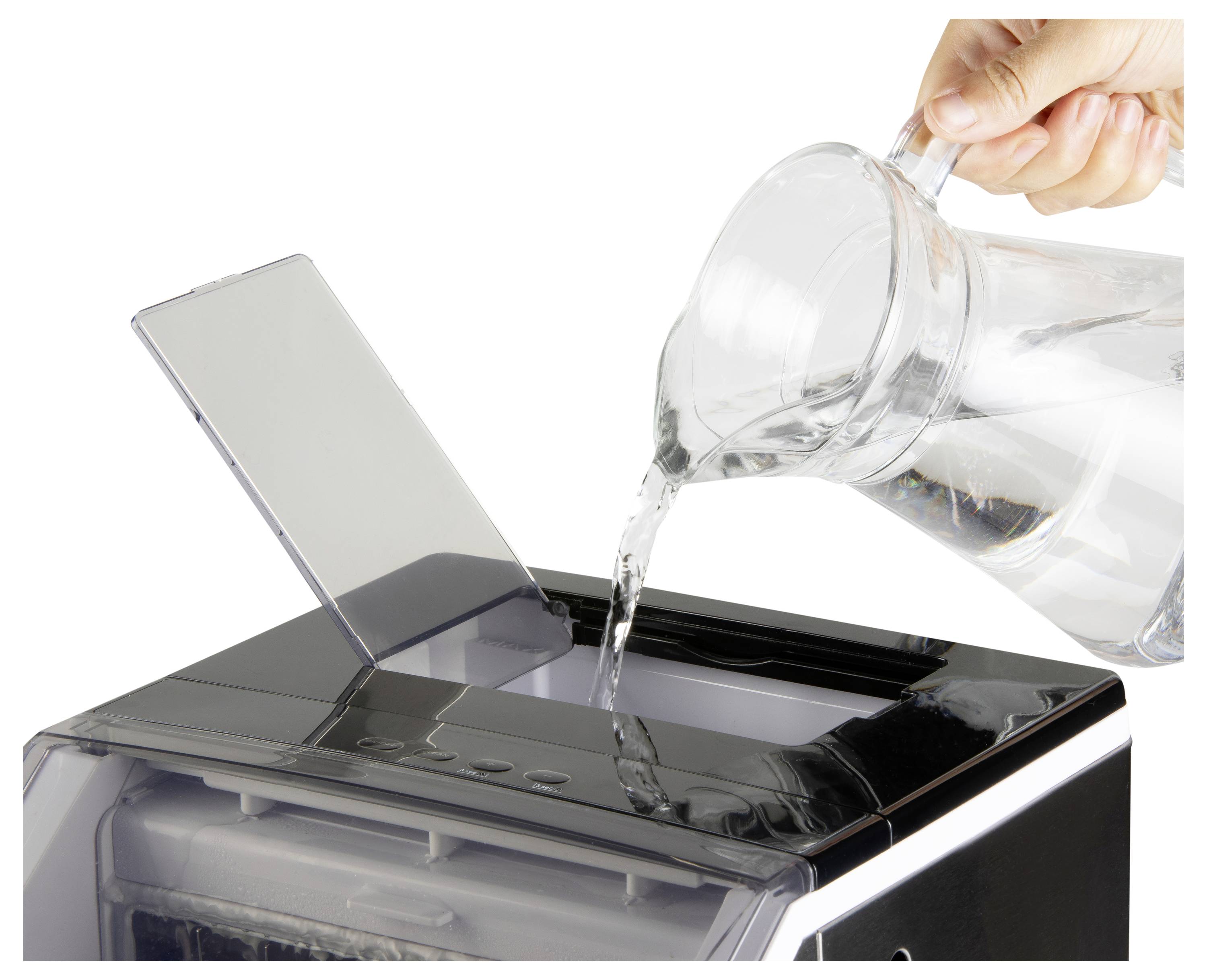 Water is being poured from a pitcher into the open top of a small countertop appliance, likely adding water to a humidifier or dispenser.