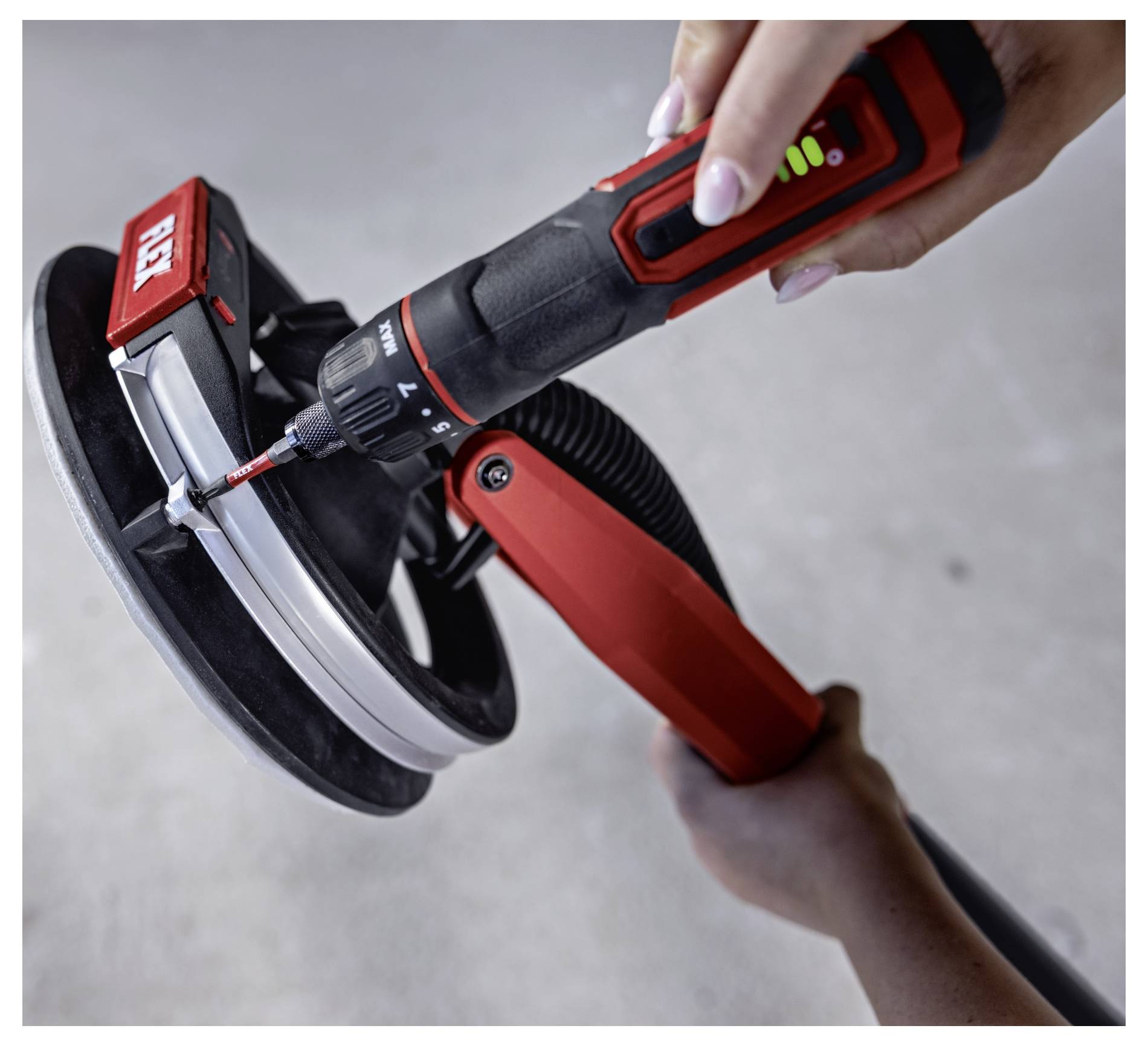 Hands use a cordless power screwdriver to fasten a red-and-black device held in a clamp, showing close-up tool assembly or repair.