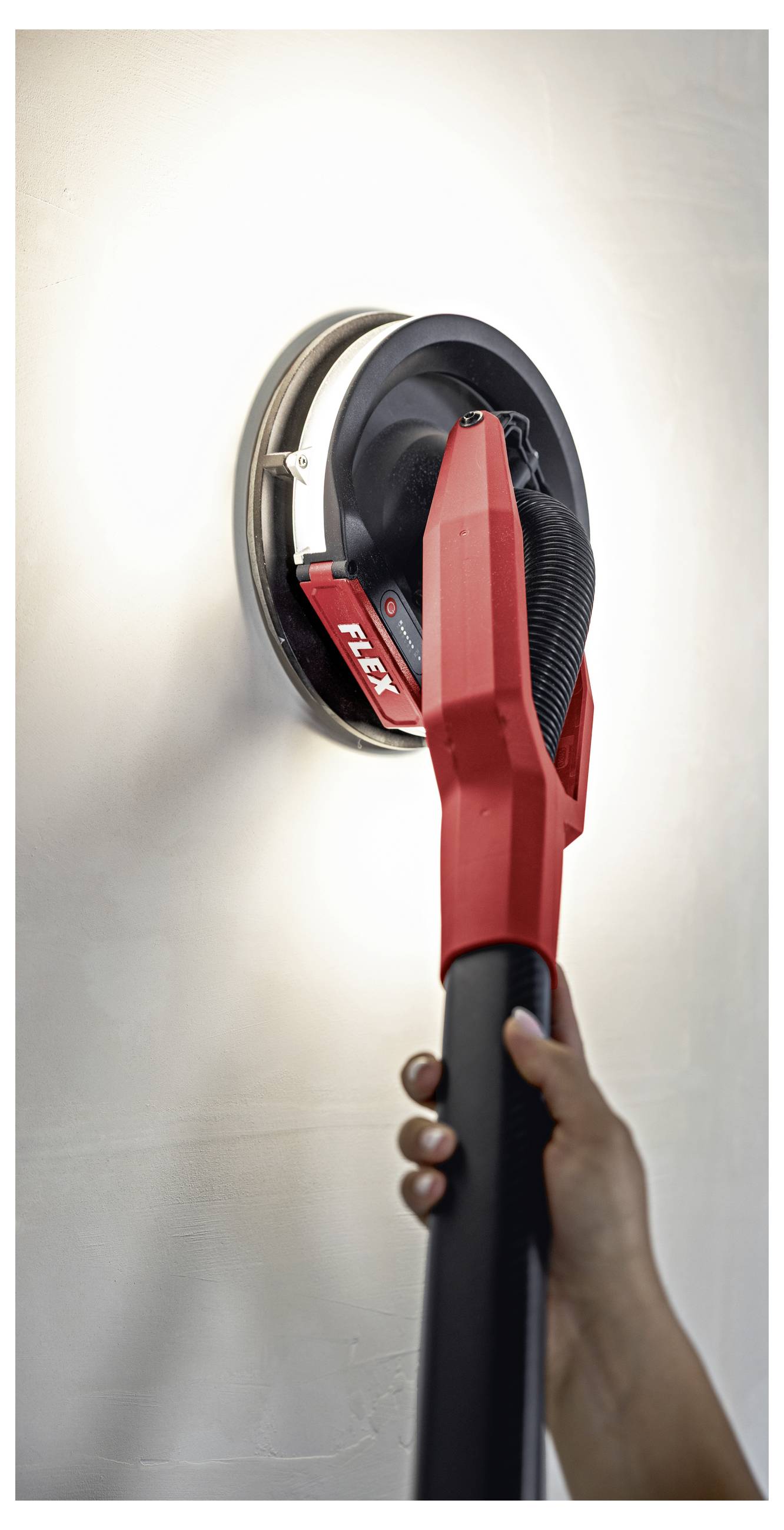 Handheld vacuum cleaner head pressed against a wall, cleaning a light-colored surface.