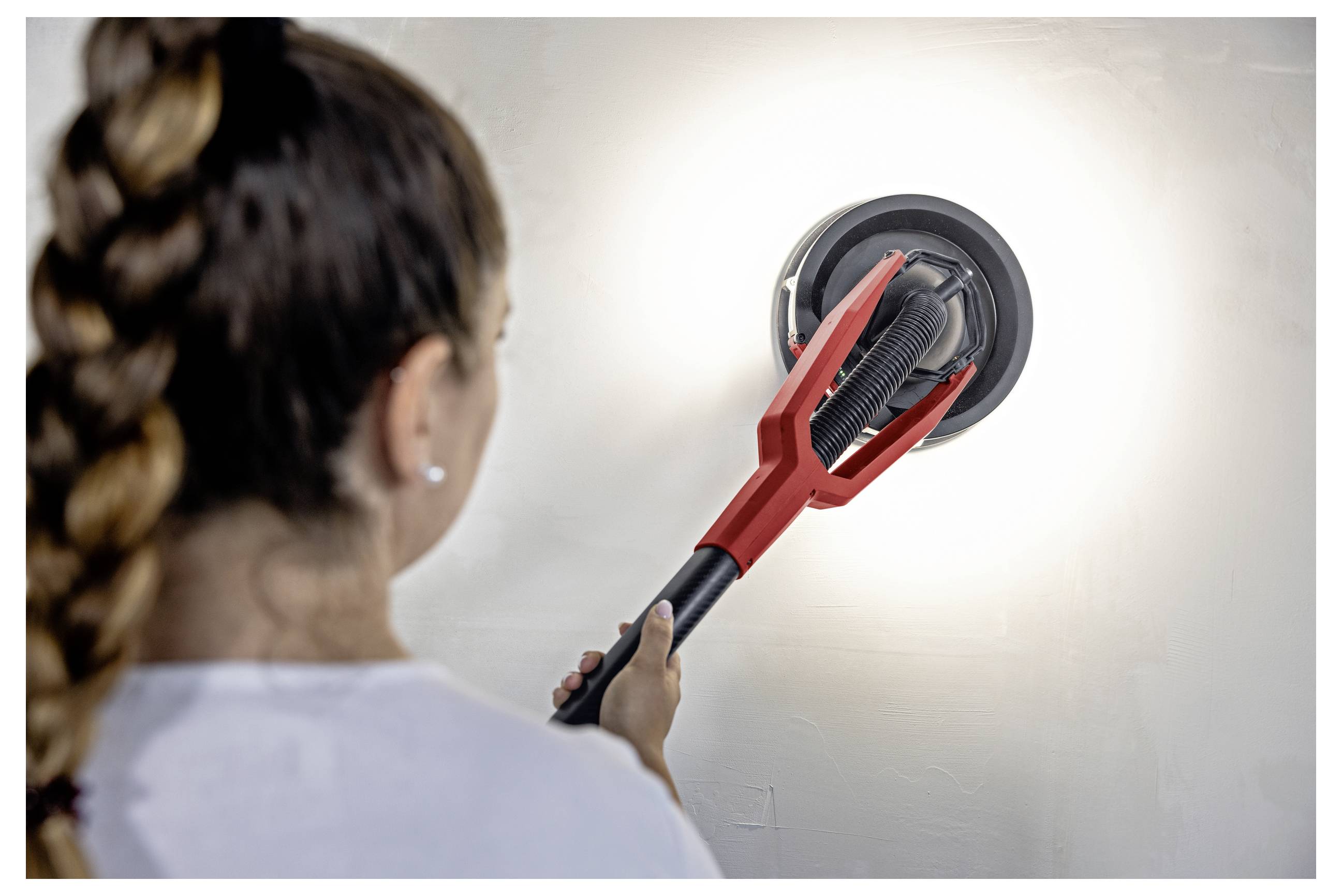 Person using a red telescoping duster to clean a round wall or ceiling light fixture.