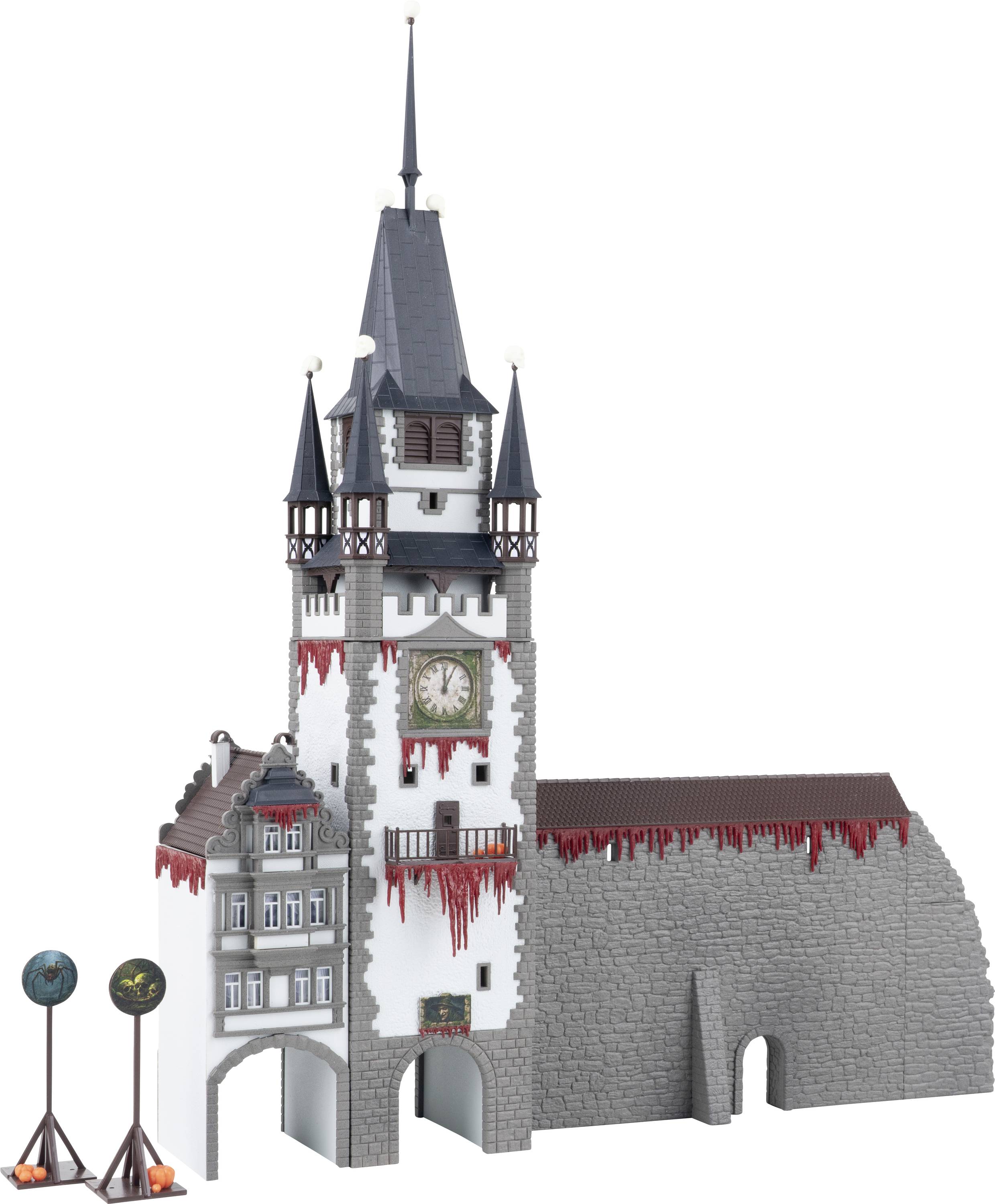 A model of a gray stone clock tower with red drips and a tall spire, attached to a castle wall and archway.