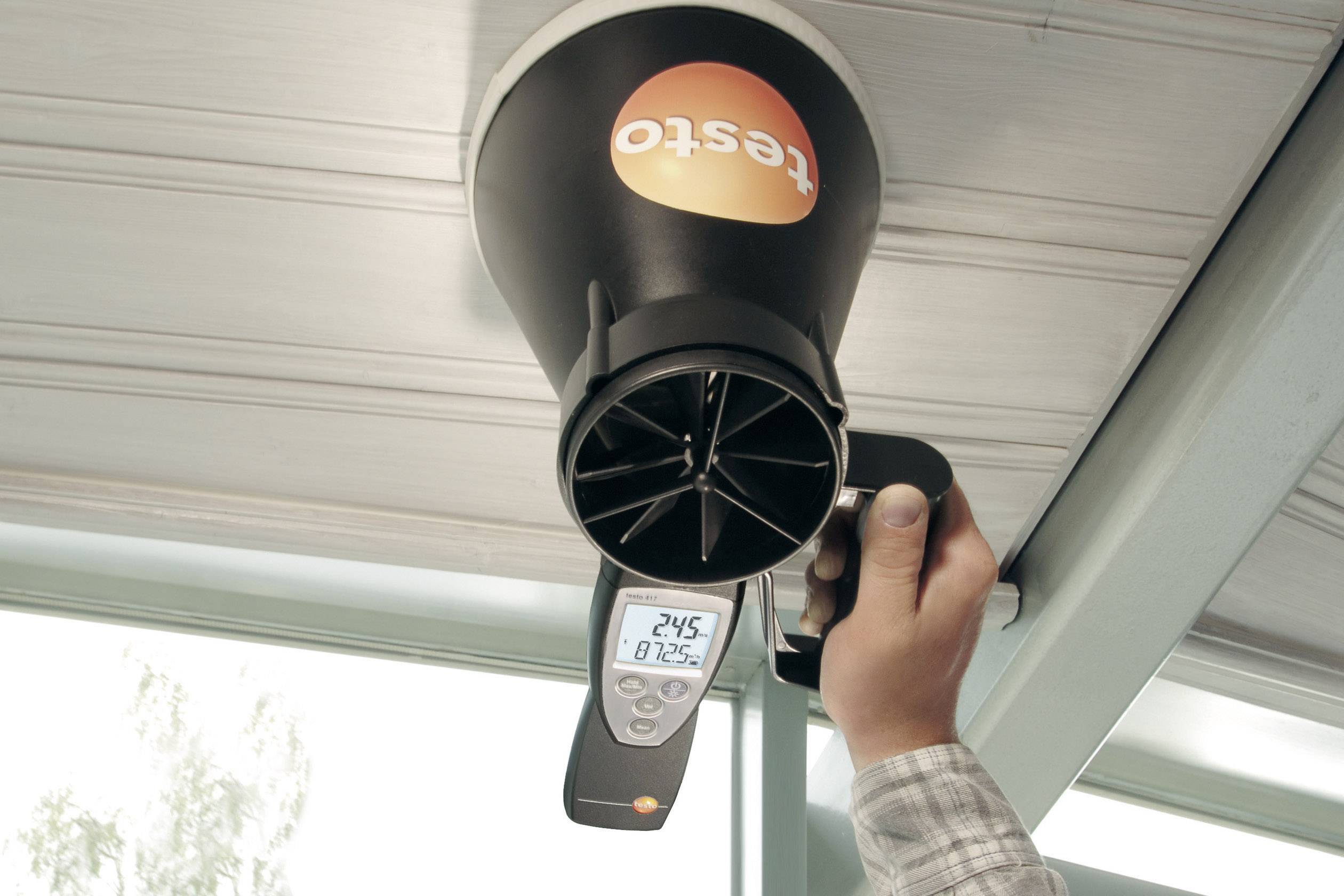 A person is holding a Testo measuring device at a ventilation outlet. The display shows 24.5 °C and 81.2% humidity.