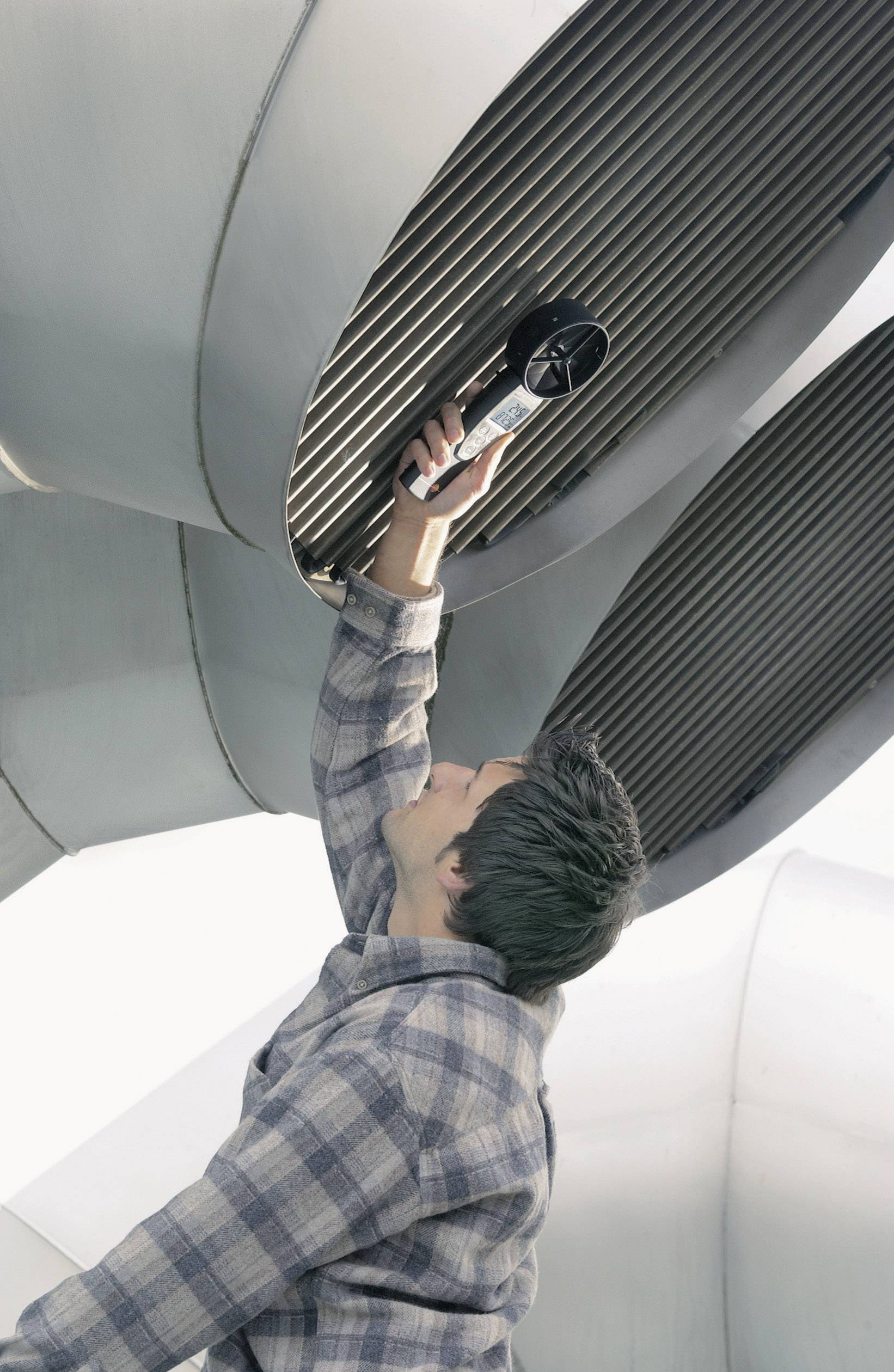 A man in a checked shirt is checking large ventilation slots with a device in an industrial environment, potentially conducting maintenance work.