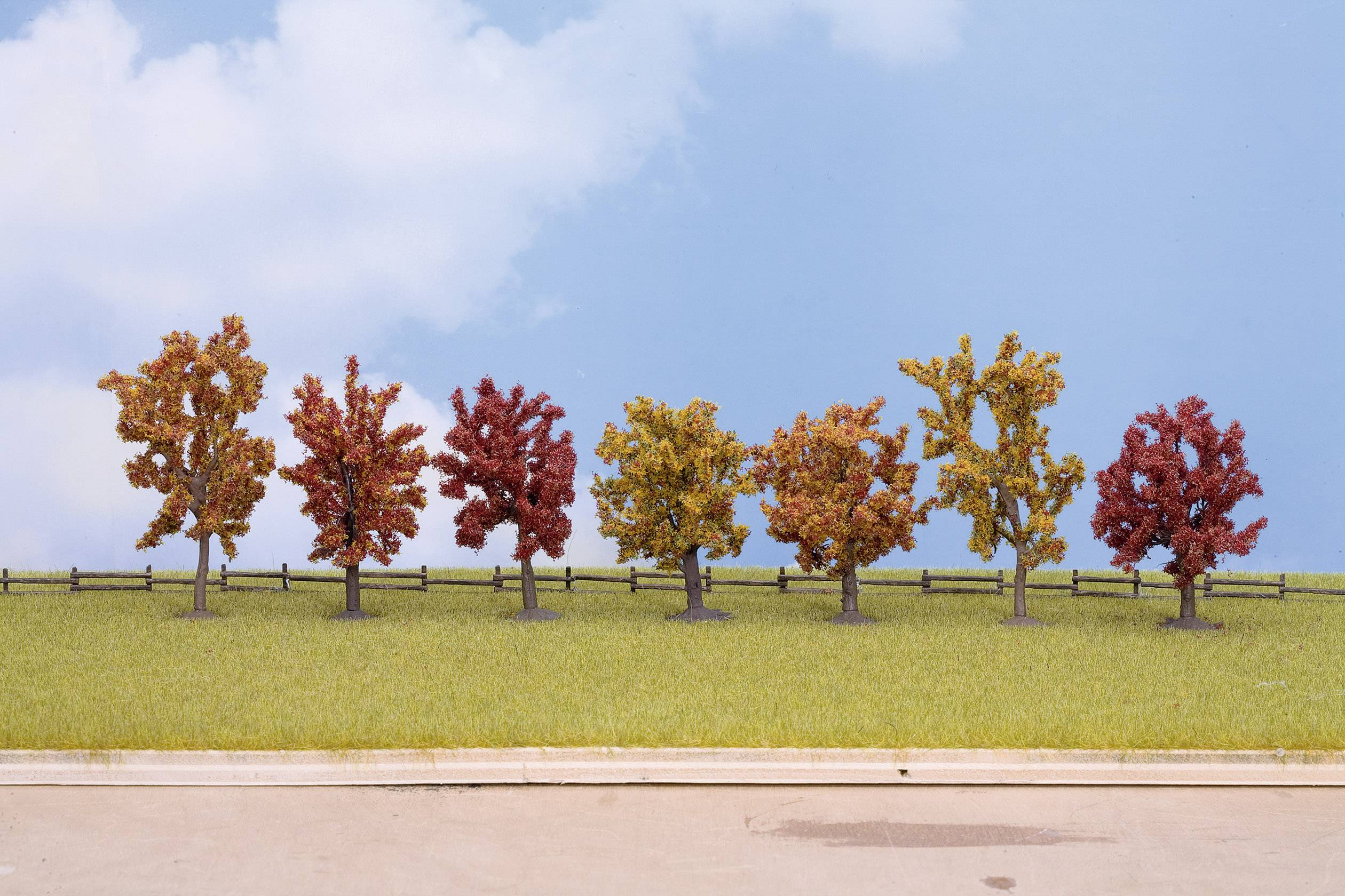 A row of trees with autumn foliage on a meadow against a blue sky with a few clouds.