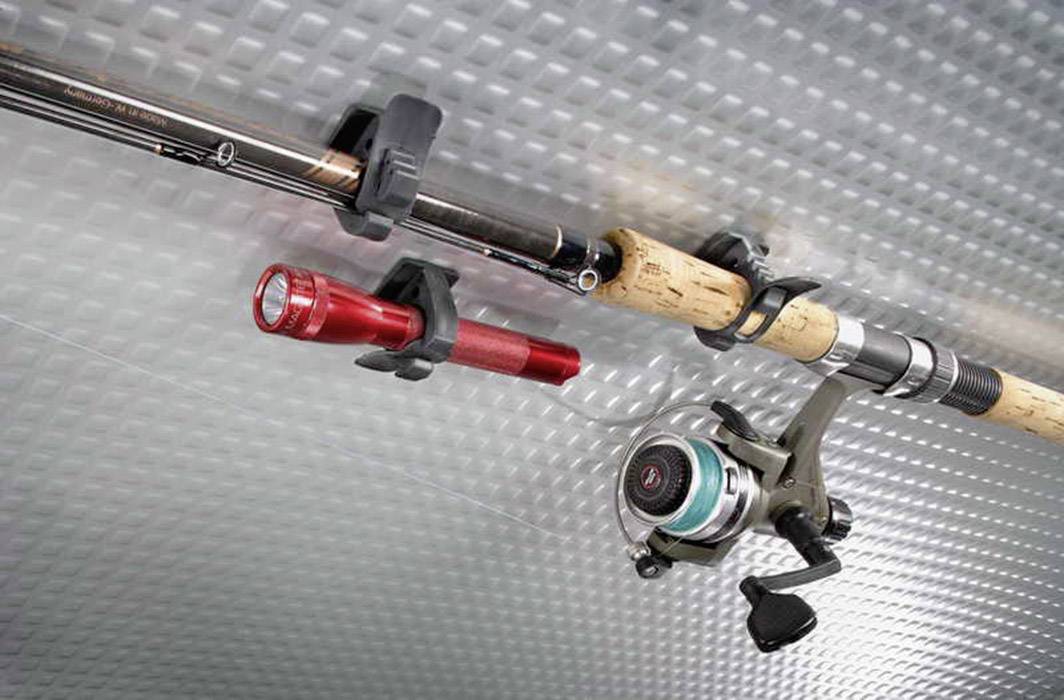 Fishing rod and torch mounted on a wall bracket, positioned on a textured metal surface.