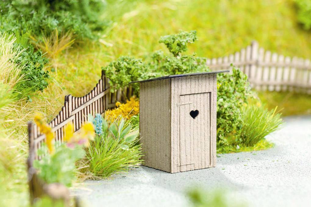 A miniature garden model shows a small wooden toilet house with a heart-shaped cut-out, surrounded by plants and a fence.