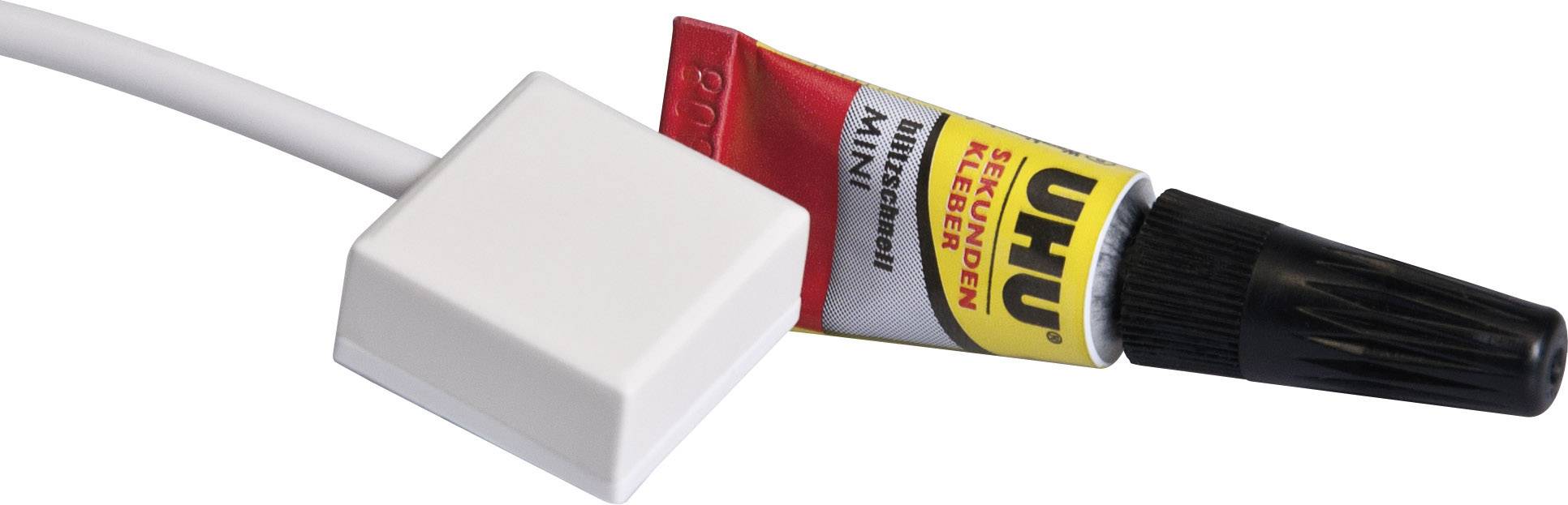 A white, square button connected to a cable lies next to a small tube of UHU instant adhesive.