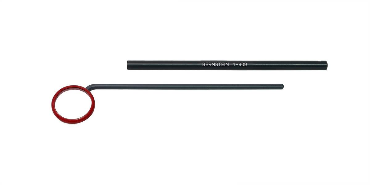 A black pen and a ring-shaped tool with a red border are lying next to each other. The pen is inscribed with 'BERNSTEIN 1-1999'.