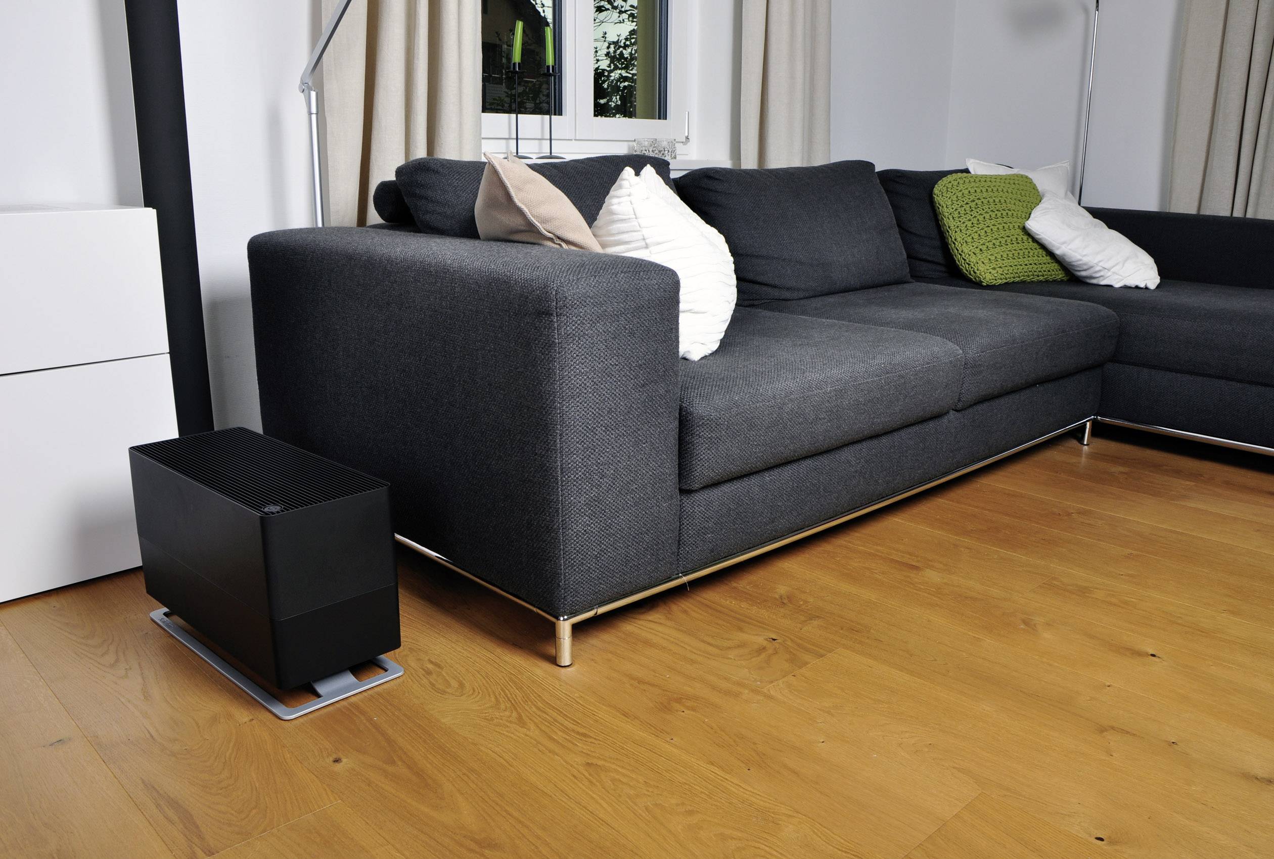 Dark grey sofa in a modernly furnished living room with wooden flooring. A black device sits to the left of the sofa.