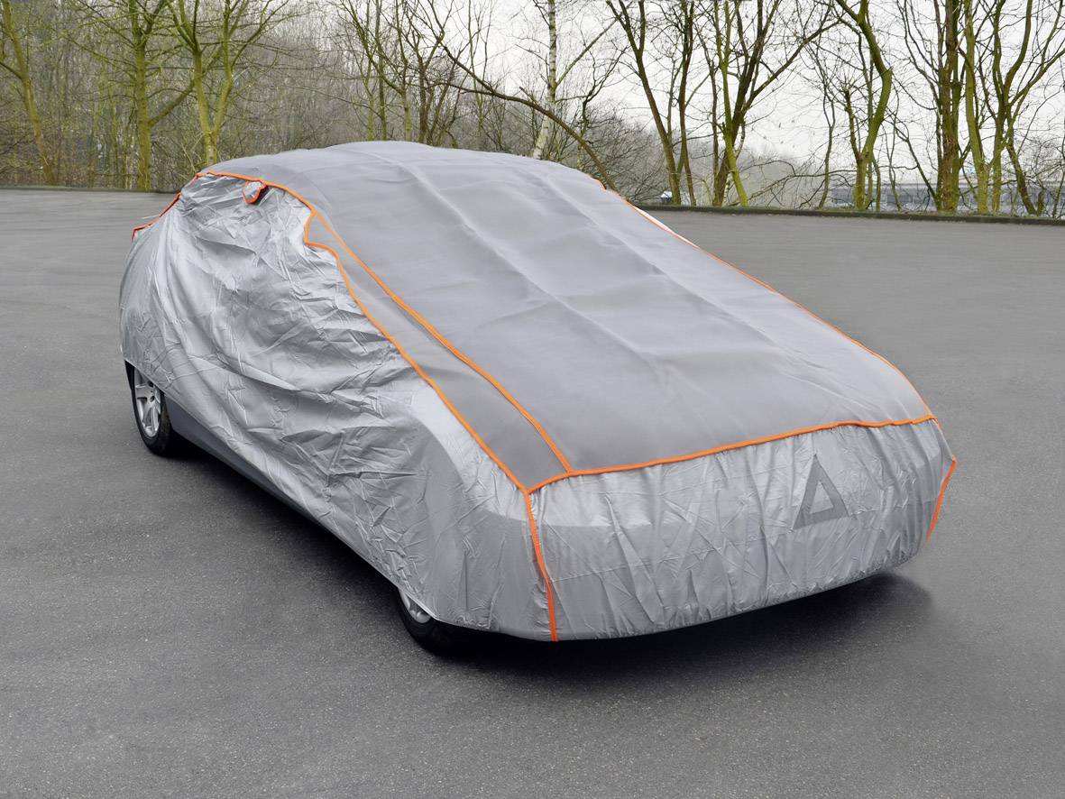 A car is parked on a car park and is covered with a grey tarpaulin. Trees are visible in the background.