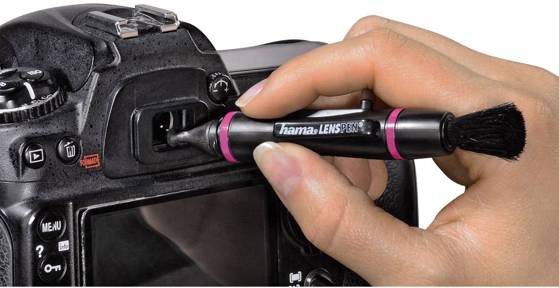 A hand is cleaning the viewfinder of a camera with a specialised lens cleaning brush. The focus is on caring for the camera optics.
