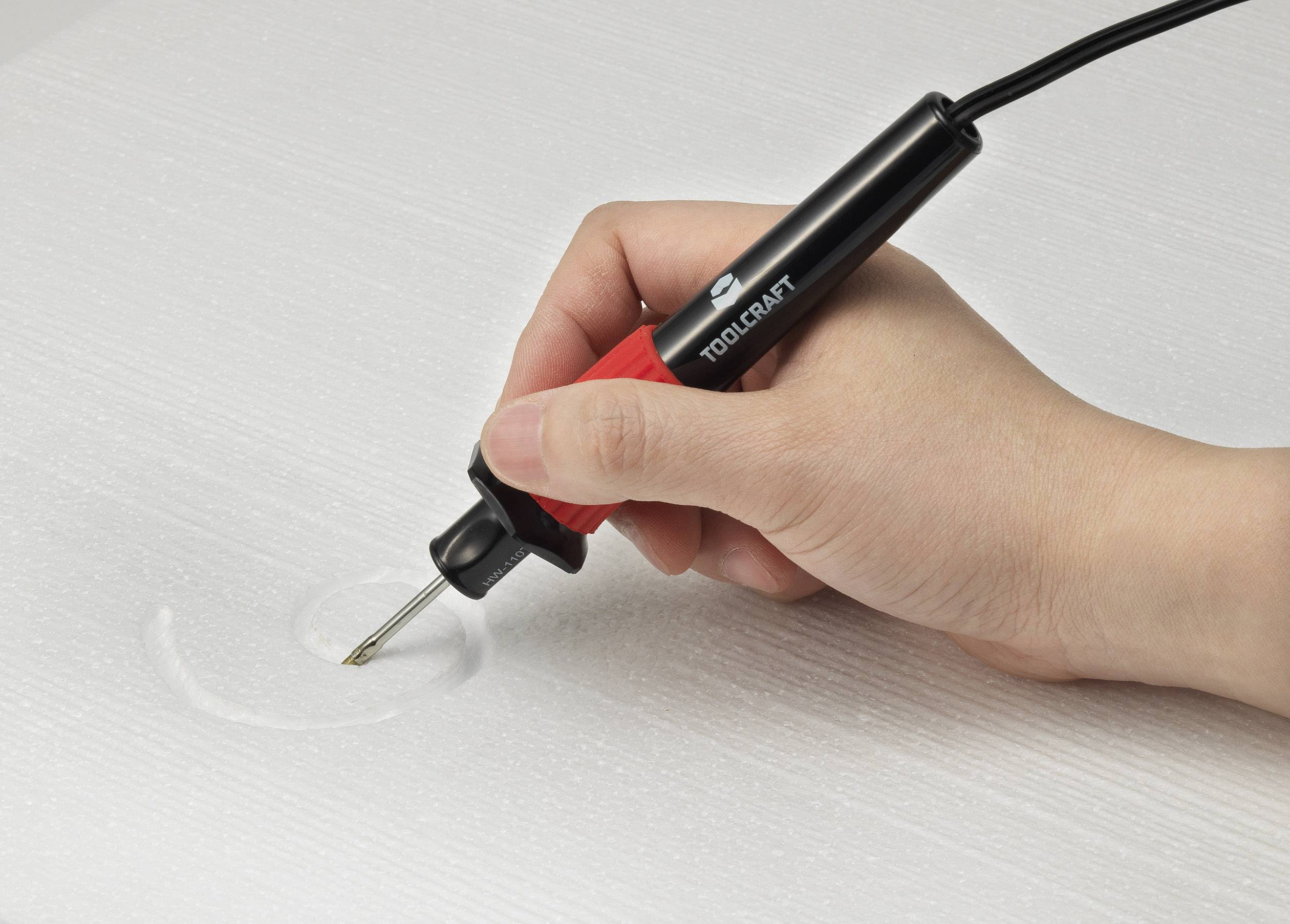 A hand is holding a soldering iron, pressing it into a white foam. The iron is red and black, while the foam slightly gives way.