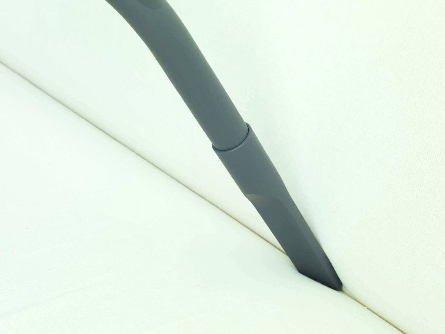 A vacuum cleaner hose is being used to clean the corner of a white sofa.