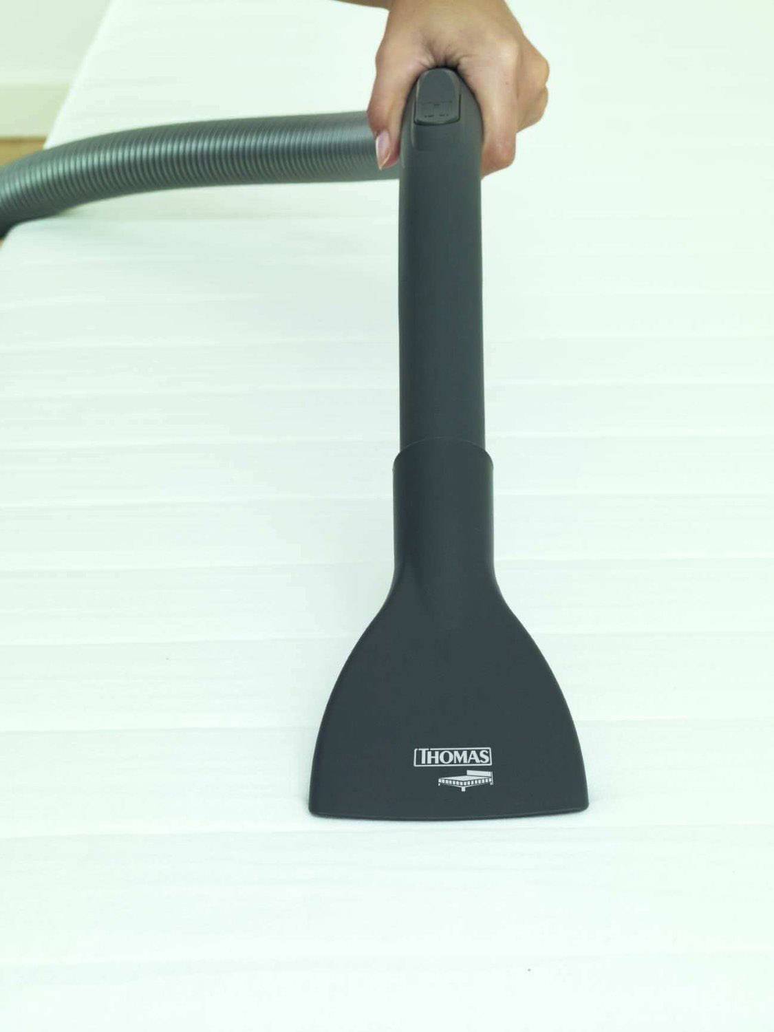 A hand is holding a vacuum cleaner hose and cleaning a white surface with a nozzle.