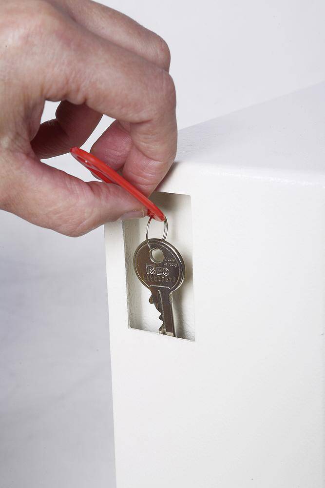 A hand is inserting a key with a red keyring into a lock on a white piece of furniture.