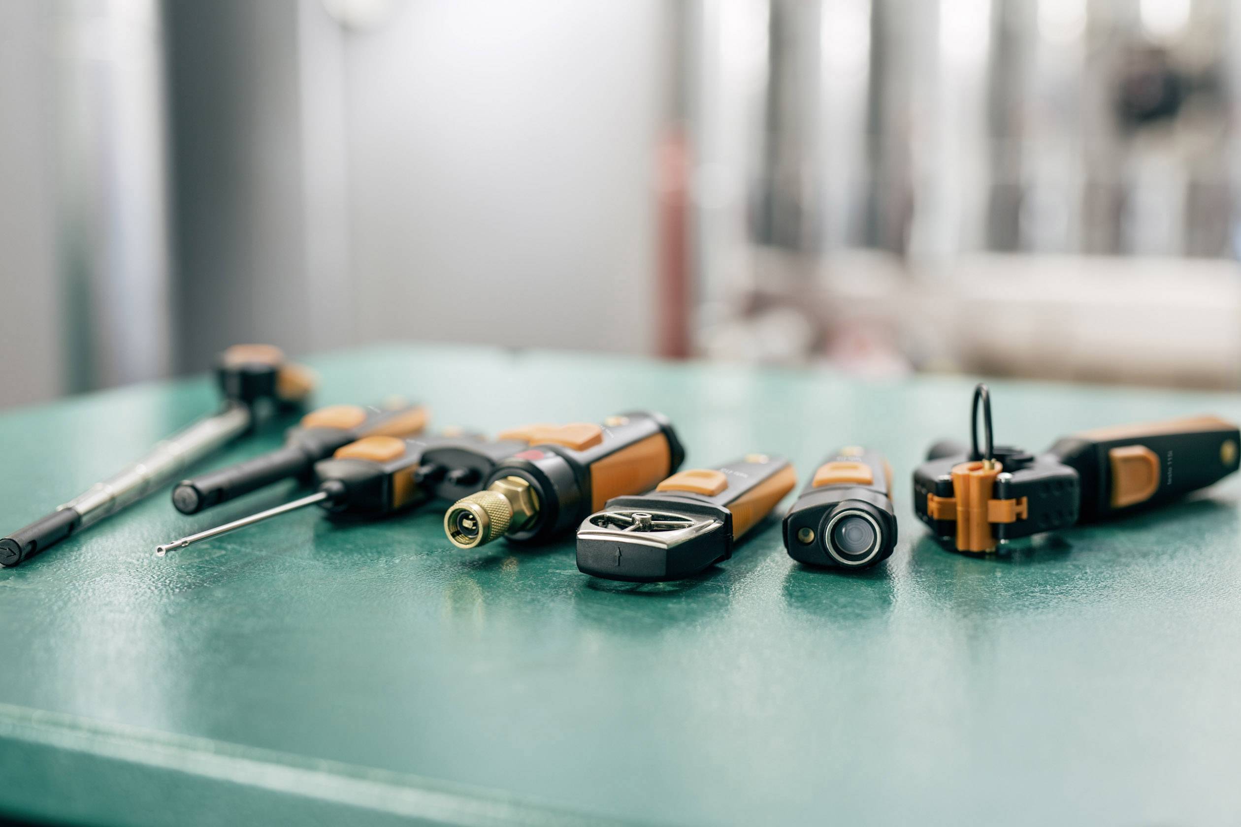 Various orange and black tools lie on a green table. The tools are arranged in a line and partially blurred.
