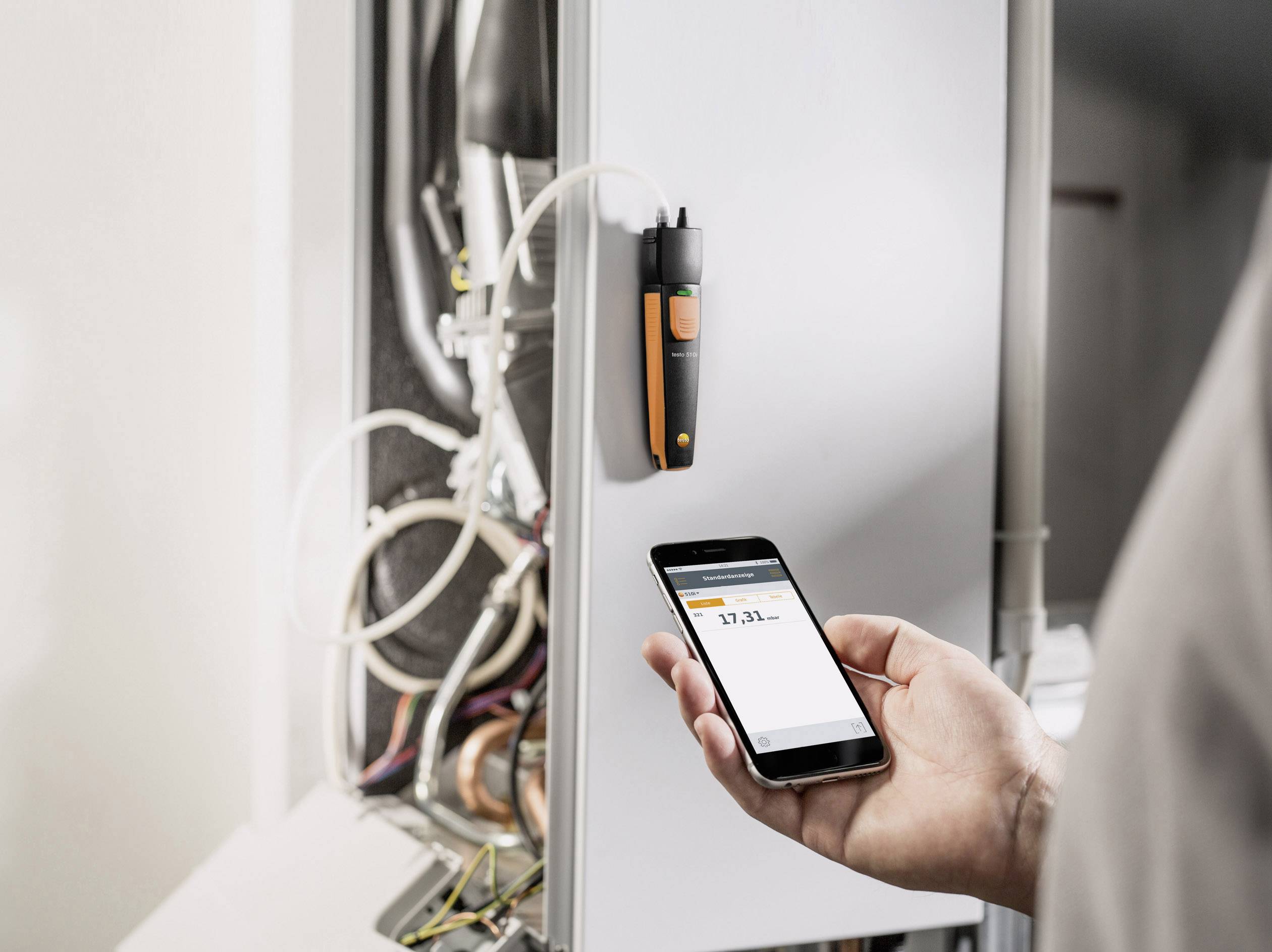 A person is measuring the values of a boiler using a smartphone and a connected sensor. Numbers are visible on the screen.