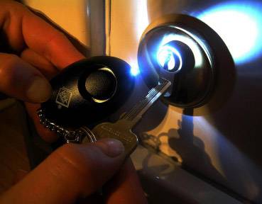 A hand is holding a glowing keyring and a key being inserted into a door lock.