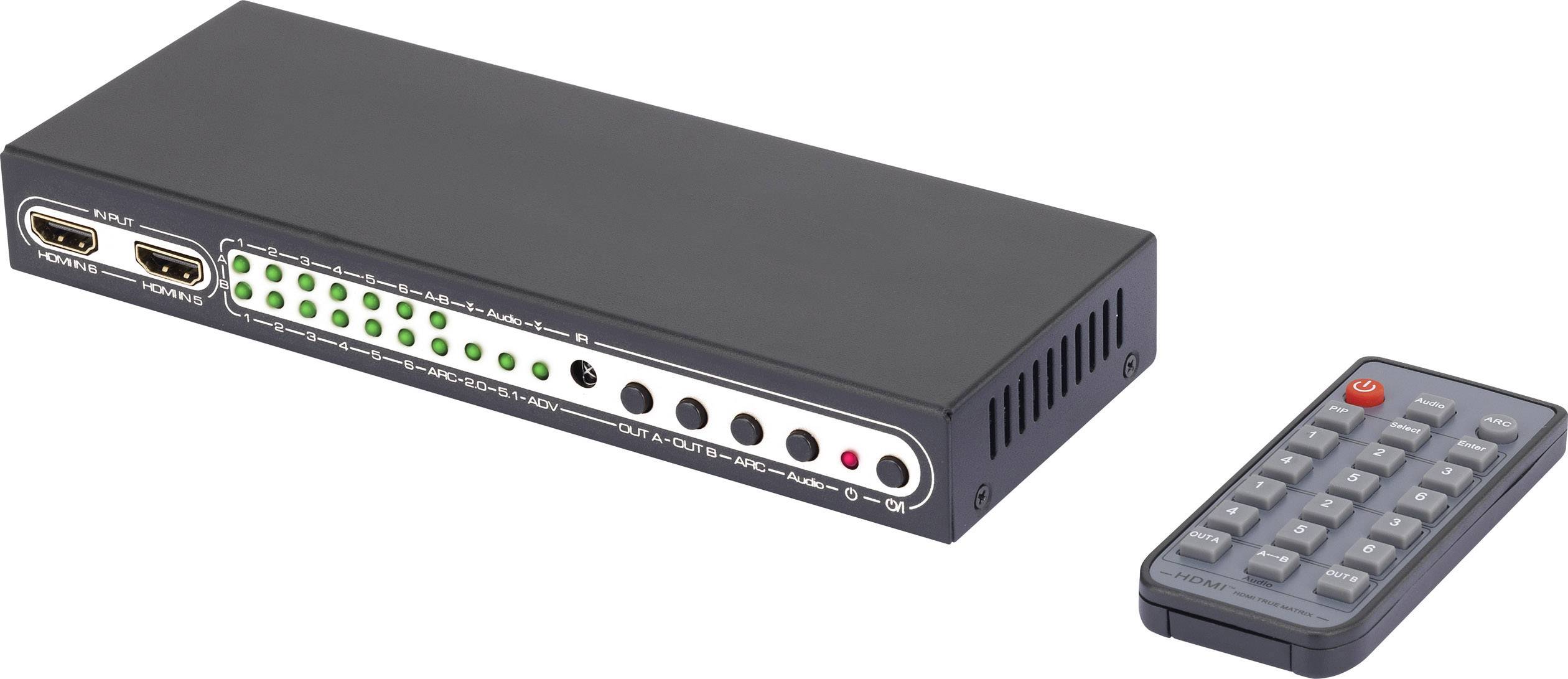 Black HDMI splitter with two ports on the left side and several green LEDs on the top surface. A remote control is positioned next to it.