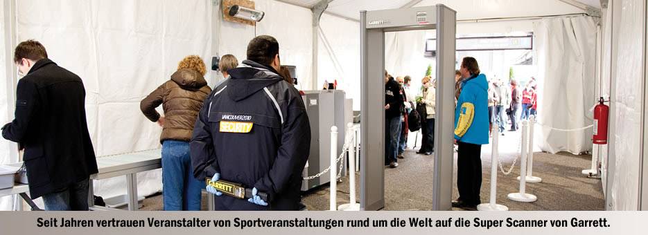People pass through security control at a sporting event, while staff monitor the scanners.