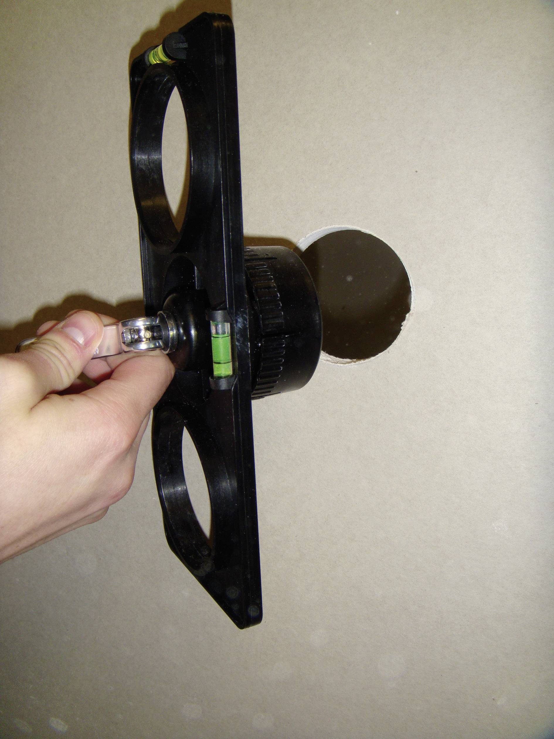 A hand holds a drill tool that is boring a round hole in a wall.