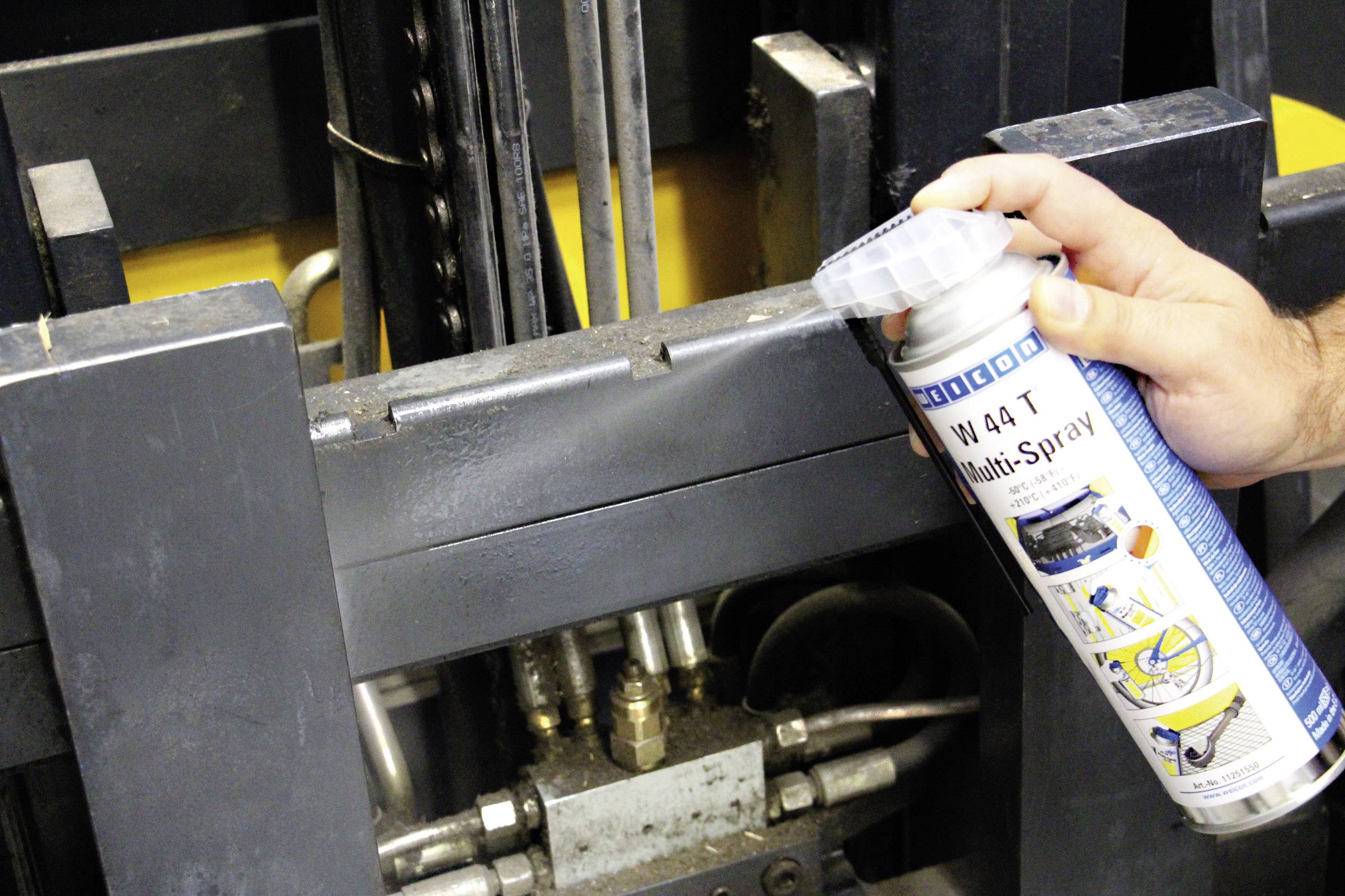 A hand sprays multi-purpose lubricant onto metal machine parts for maintenance and lubrication, ensuring smooth operation.