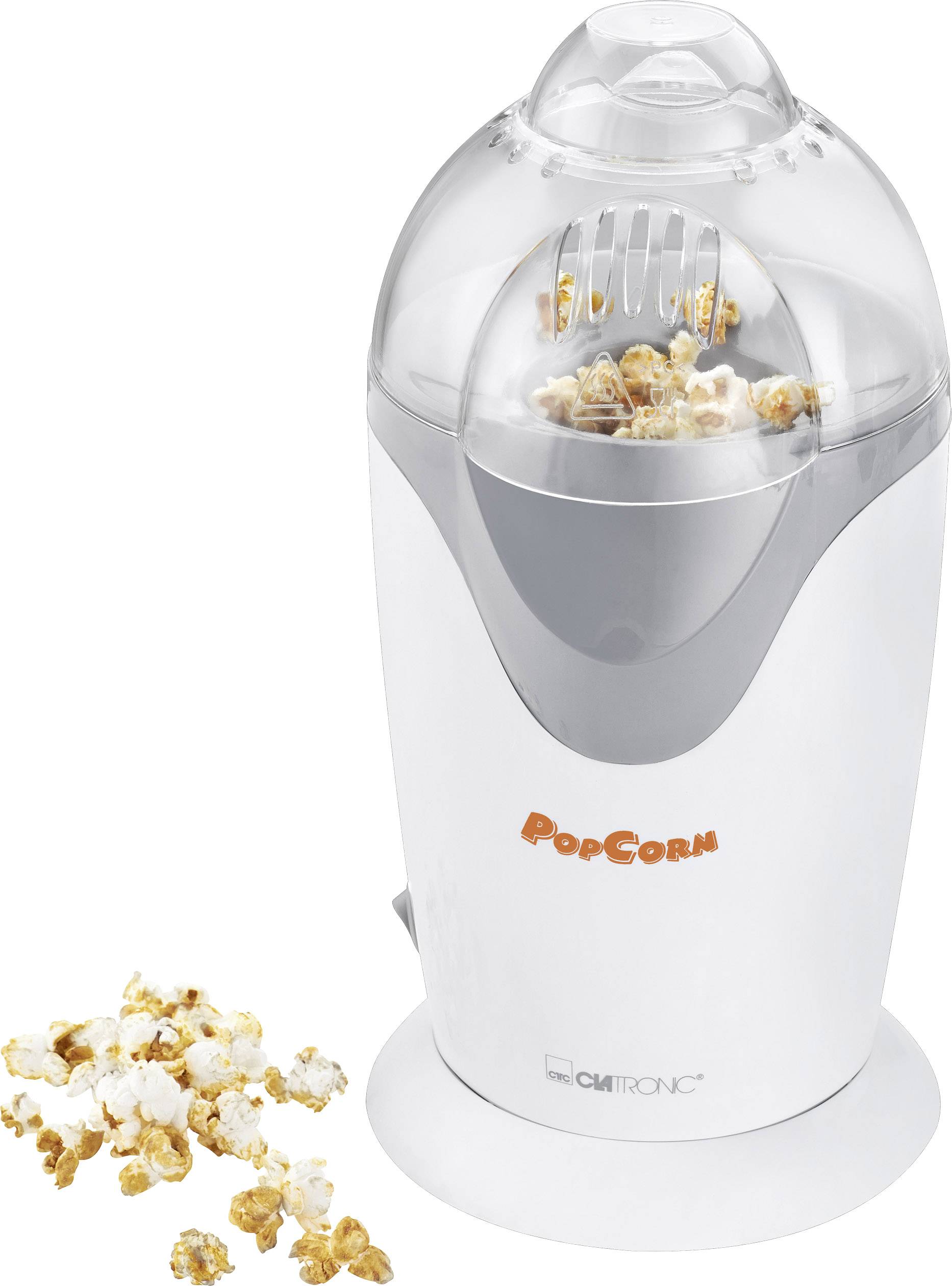Electric popcorn machine with a transparent lid. Fresh, freshly popped popcorn is visible inside. A few pieces of popcorn are lying beside it.