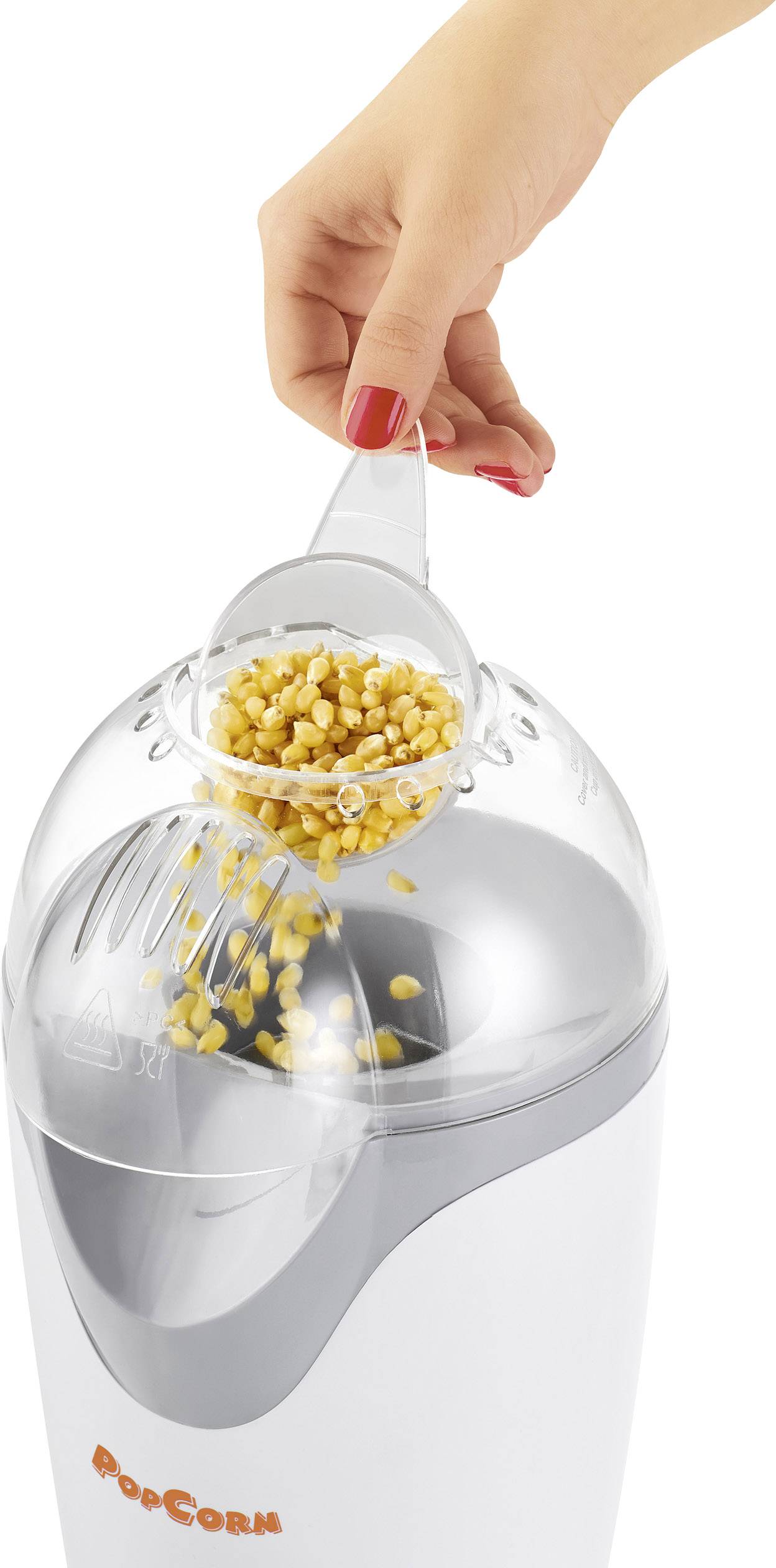 A hand fills yellow maize kernels into a white popcorn machine with a transparent lid.