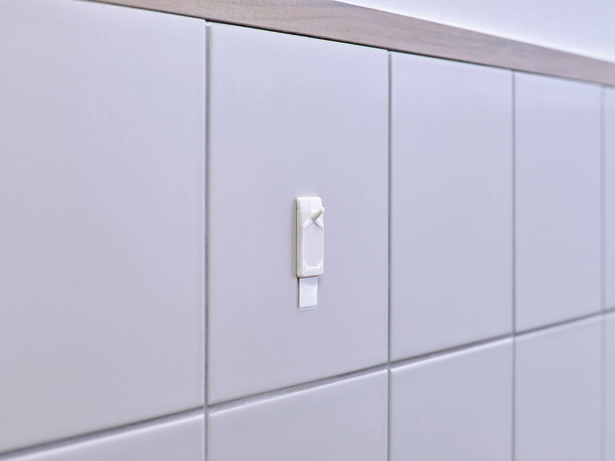 A white plastic bracket is mounted on a tiled wall. The bracket has a detached or loosely fitted band.