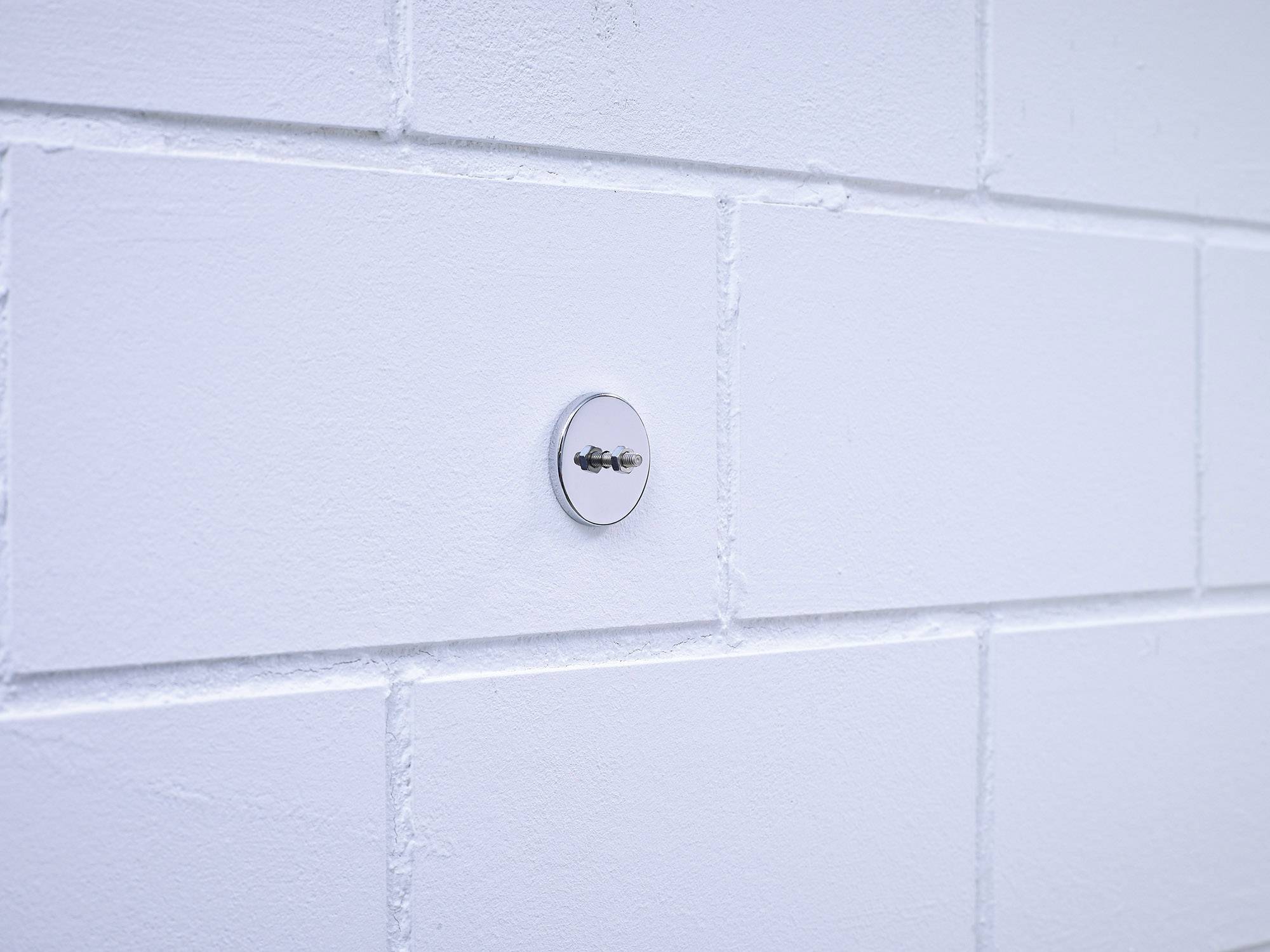 White brick wall with a shiny, round metal screw in the centre.