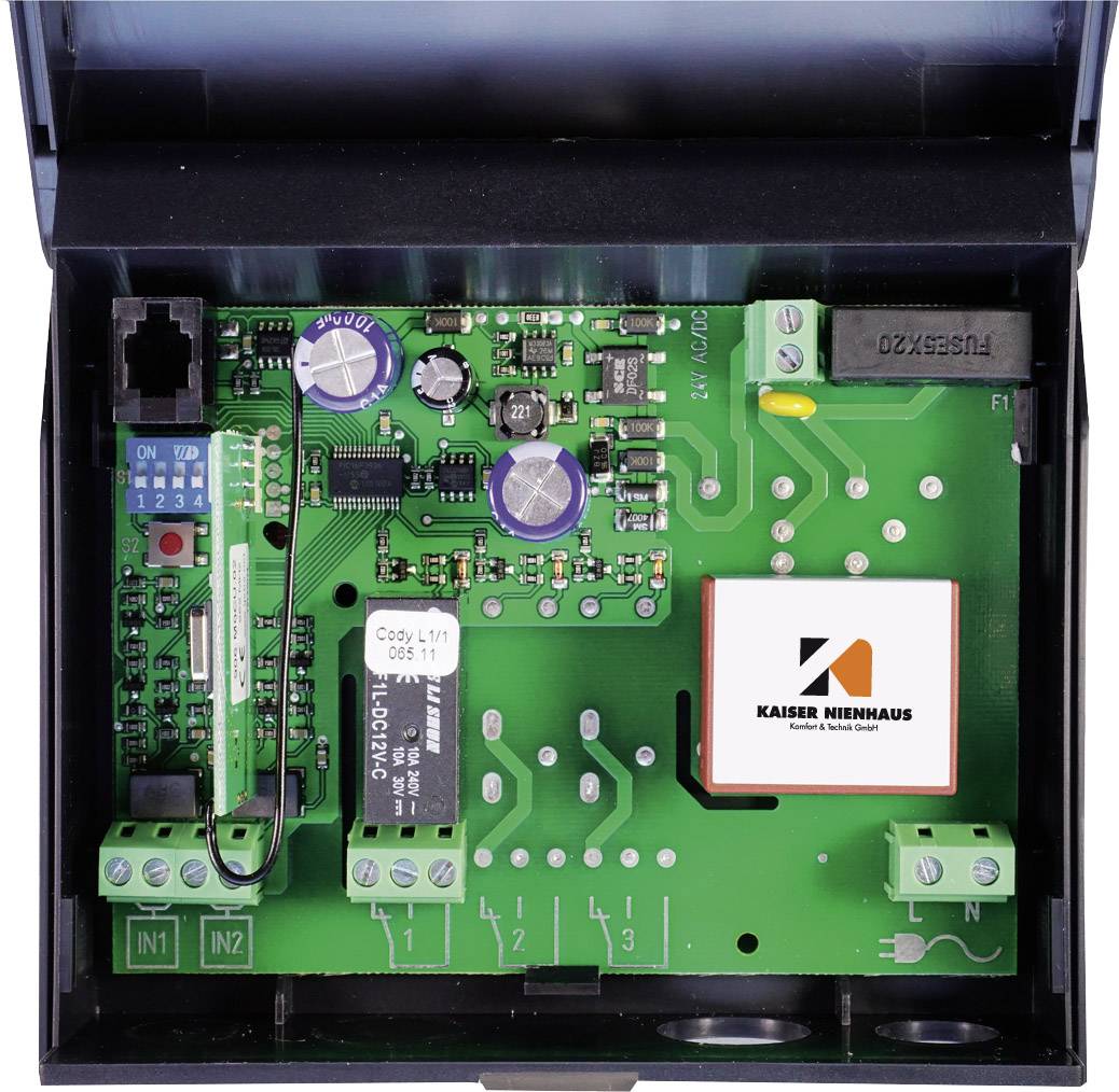 An open electronic circuit board with capacitors, resistors, and connectors on a green printed circuit board background; displaying the Kaiser Nienhaus logo.