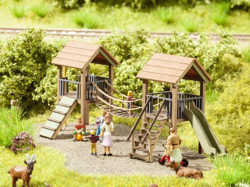 A miniature model landscape depicts a playground with a climbing structure. Several figures, including children and adults, can be seen.