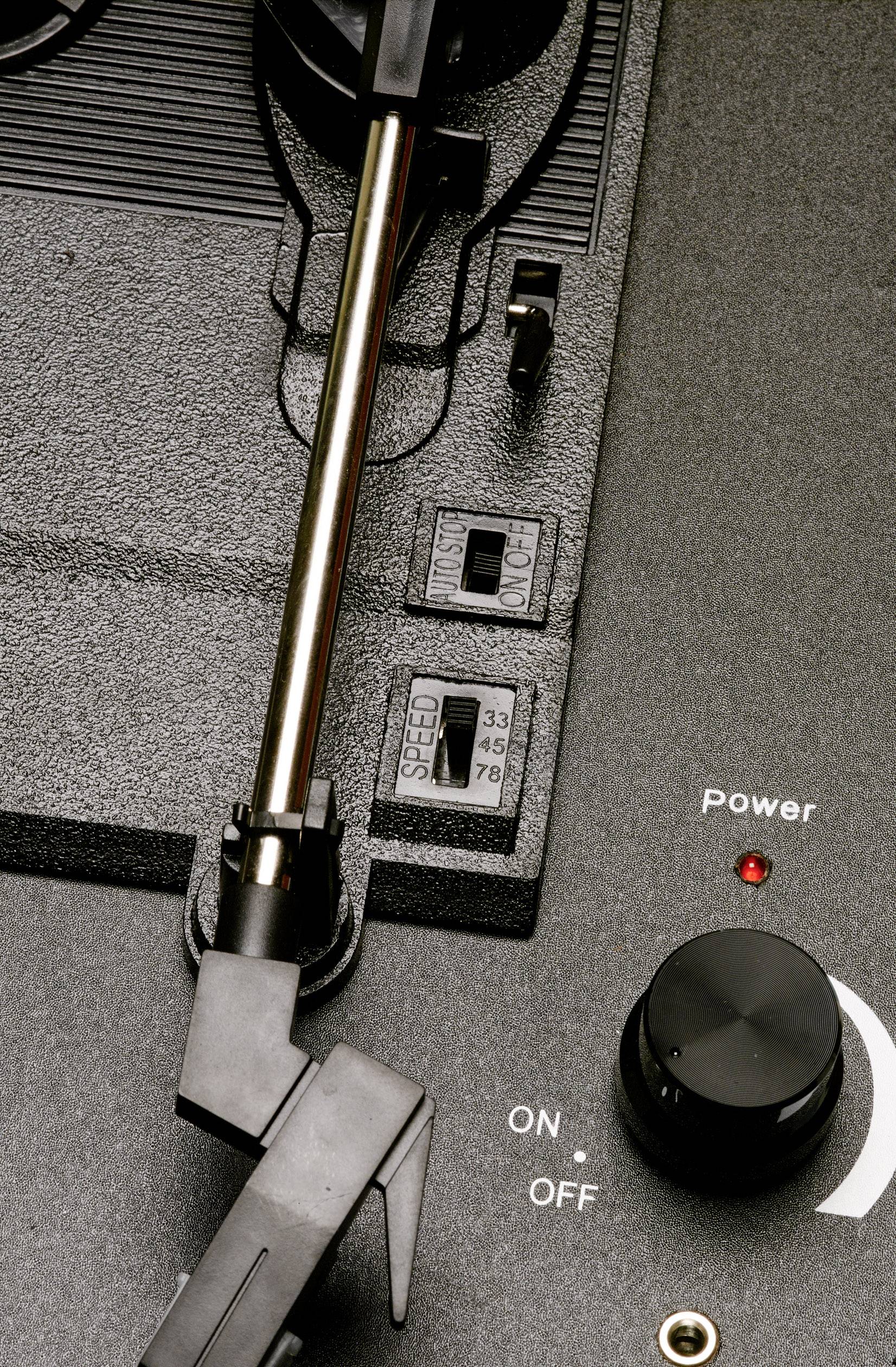 Close-up of a record player with tonearm, speed selector for 33, 45, 78 RPM and power switch.