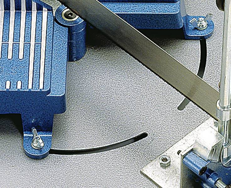 Industrial bandsaw cutting metal material on a grey surface. Two blue machine parts and a saw blade are visible.