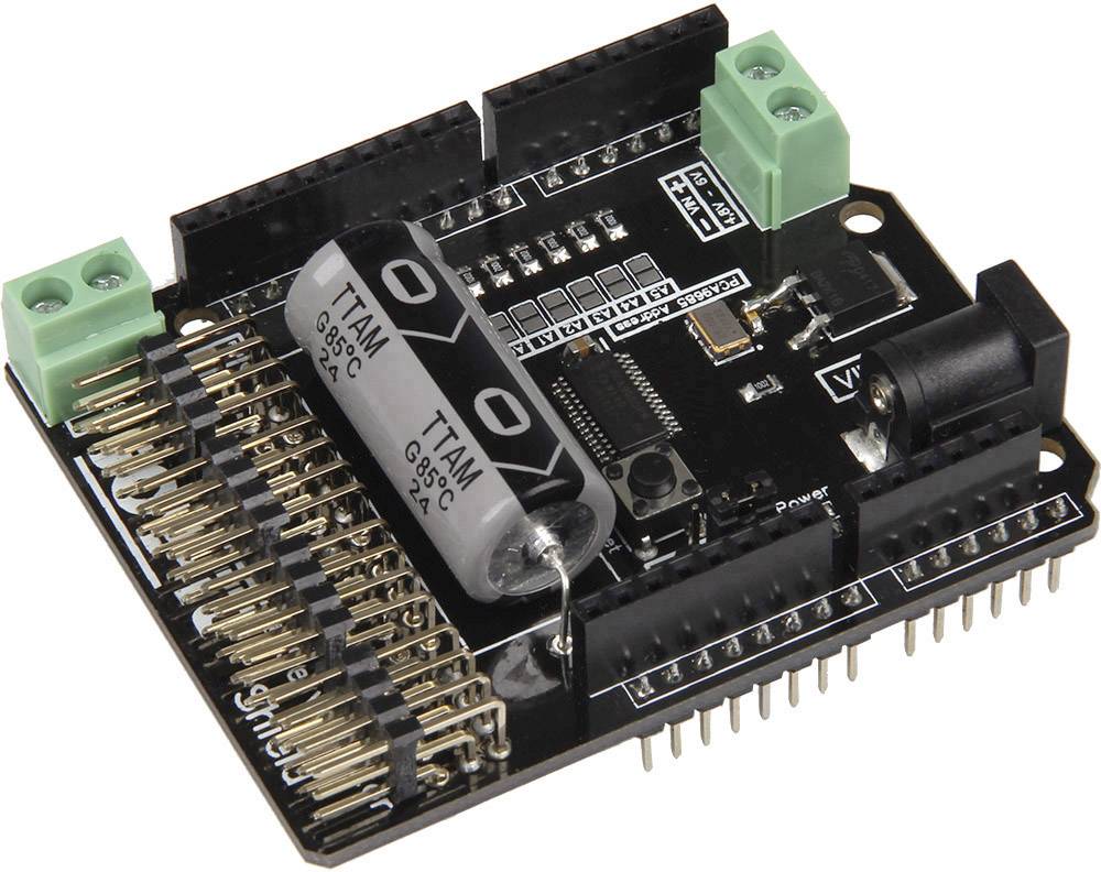 A black printed circuit board with multiple golden connectors and two large silver capacitors, along with green terminal blocks.