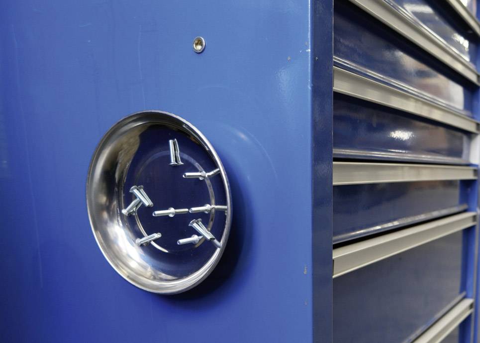 Metal screws are adhering to a round, magnetic container attached to a blue toolcabinet.