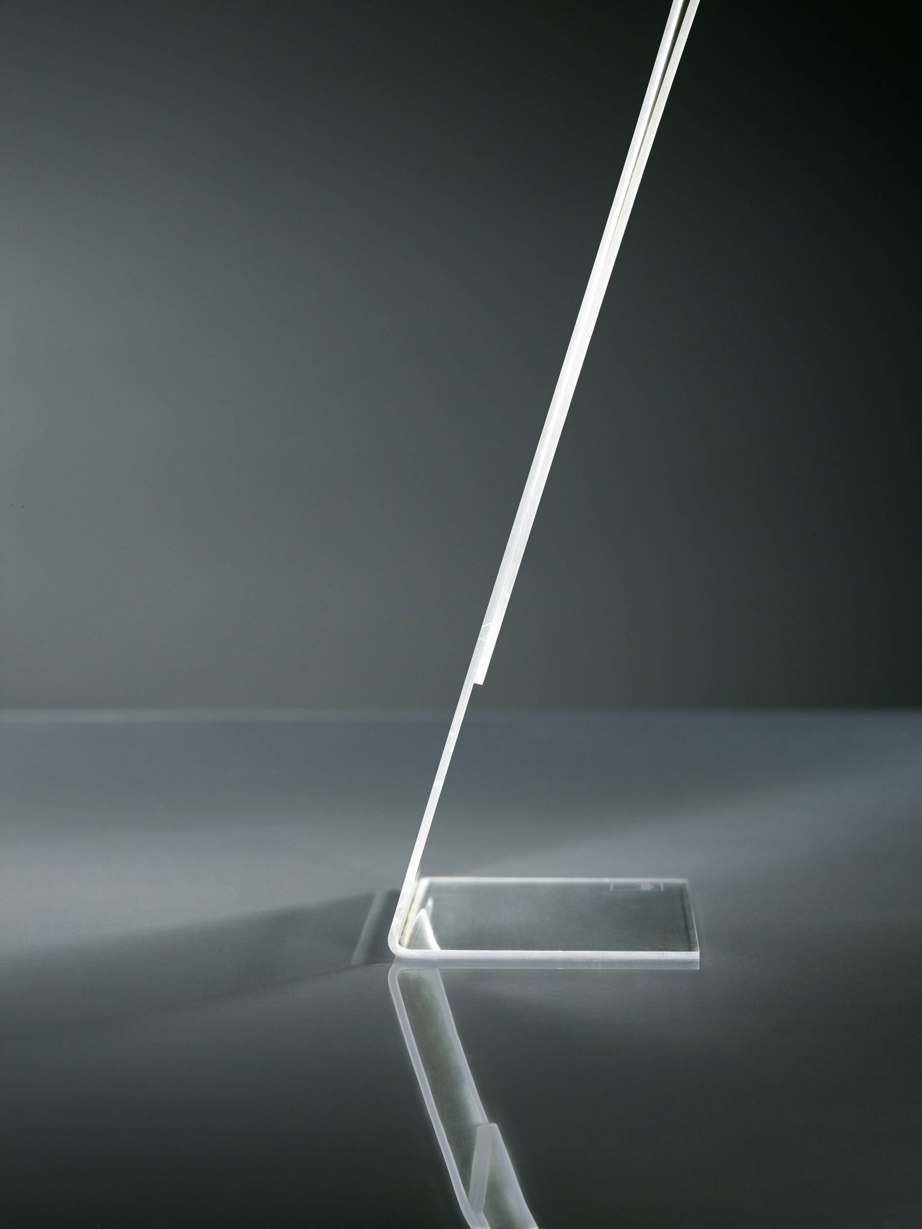 A slender, modern table lamp base made of transparent material, elegantly angled, reflecting on a glossy surface.