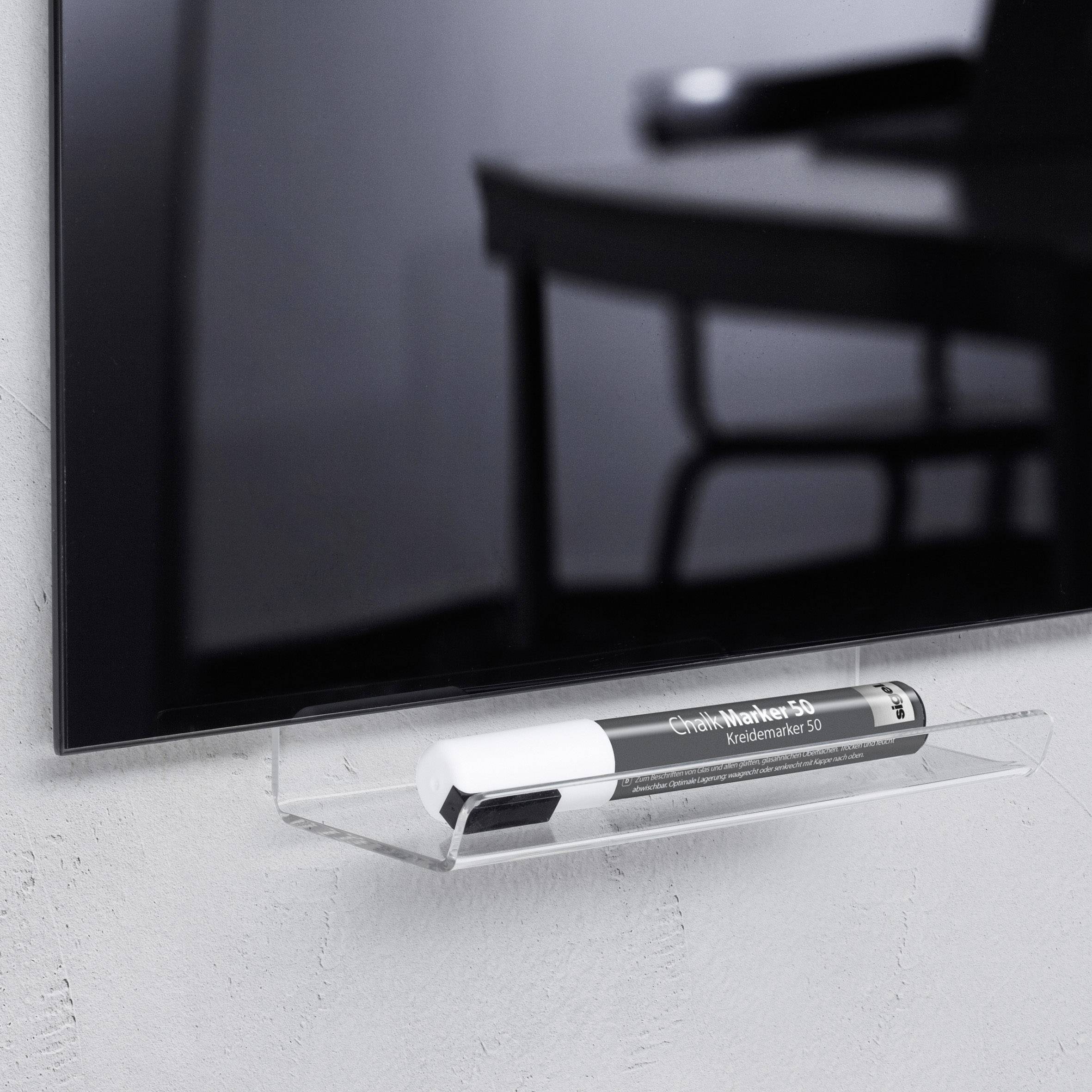 A black highlighter lies on a transparent wall shelf beneath a television, which is installed in a modern room.