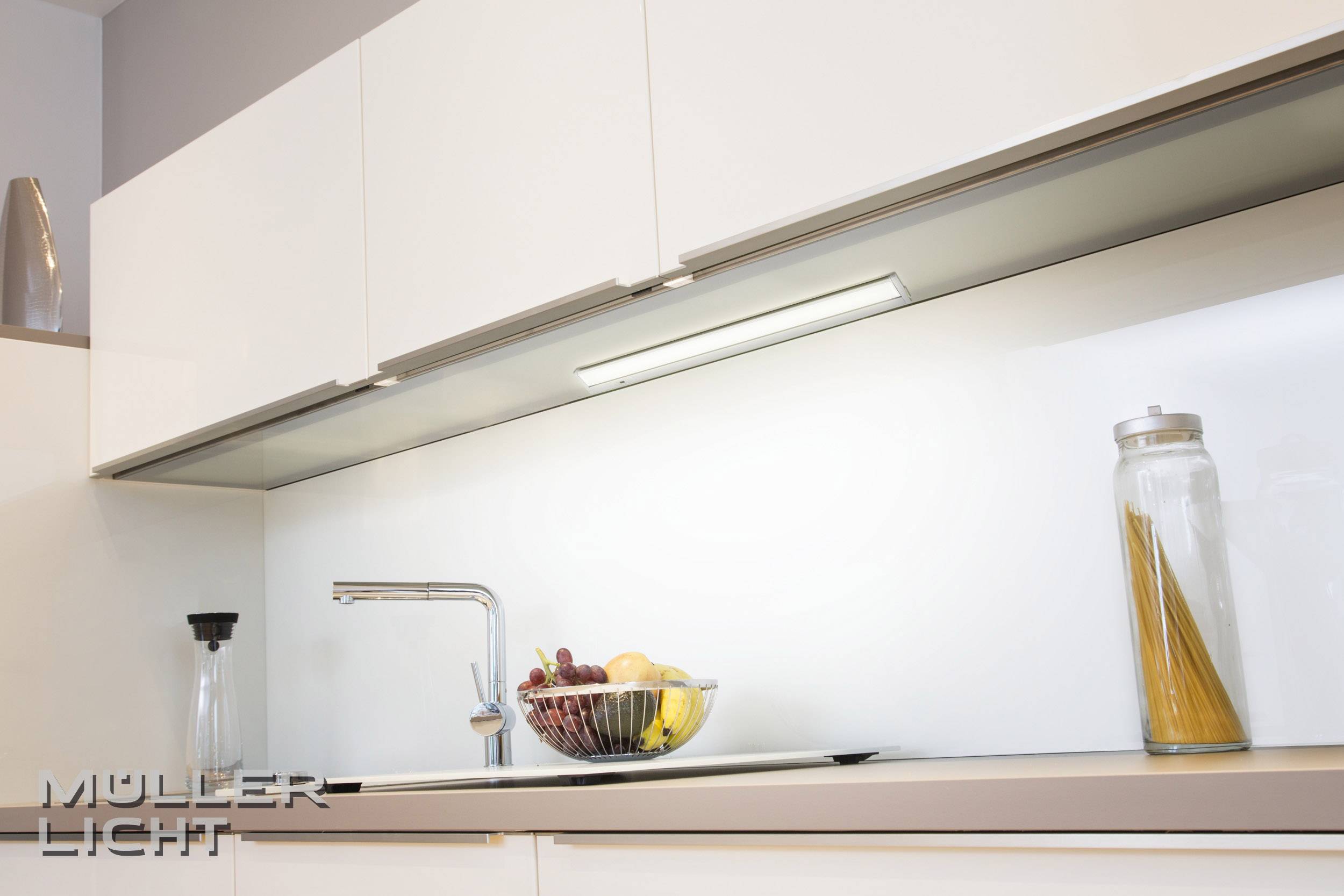 Modern kitchen with white cupboards, sink and pendant light. Fruit bowl and spaghetti jar on the worktop.